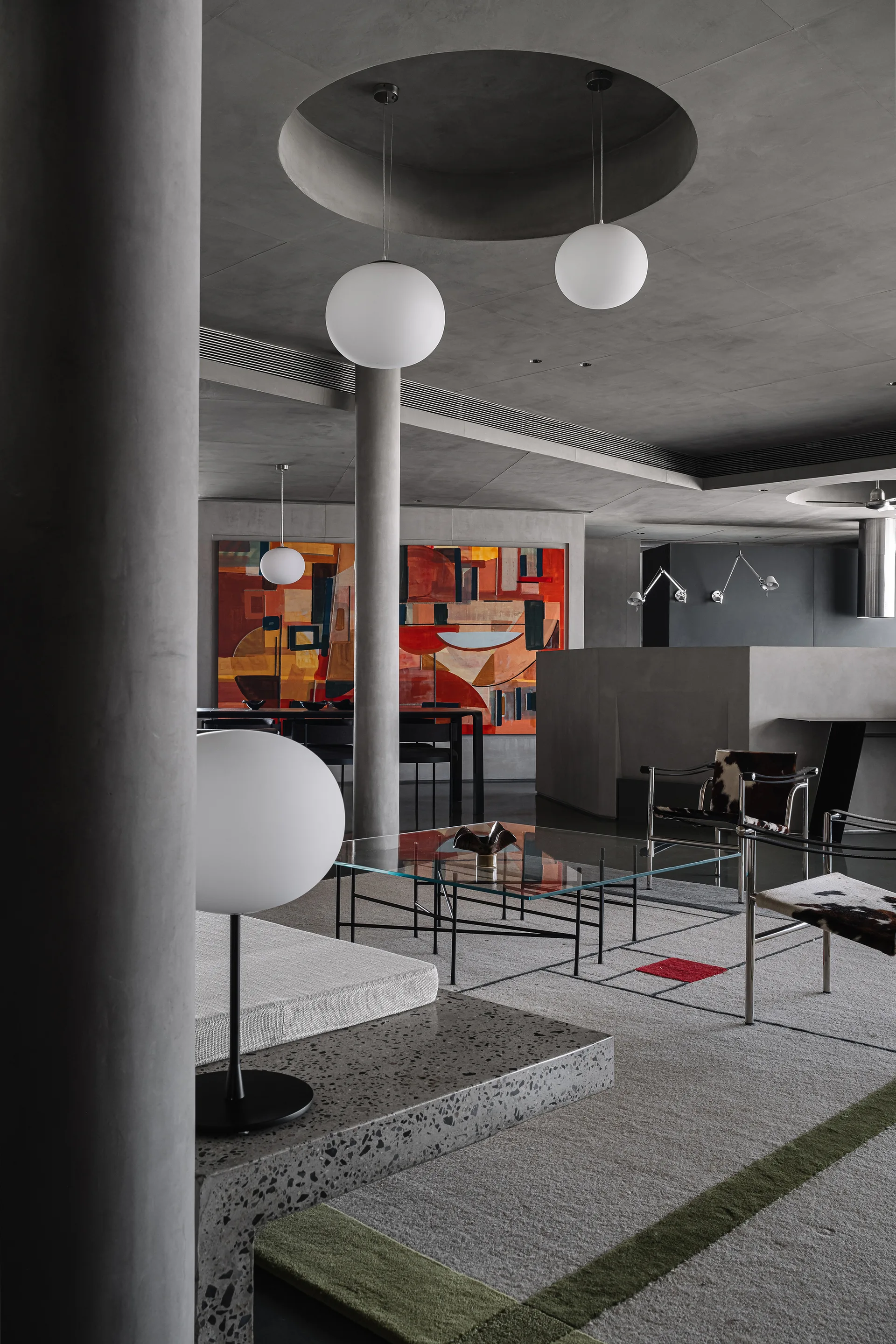A modernist living room features smooth concrete pillars, white globe pendant lights, cowhide armchairs, a glass coffee table, and a large abstract painting.