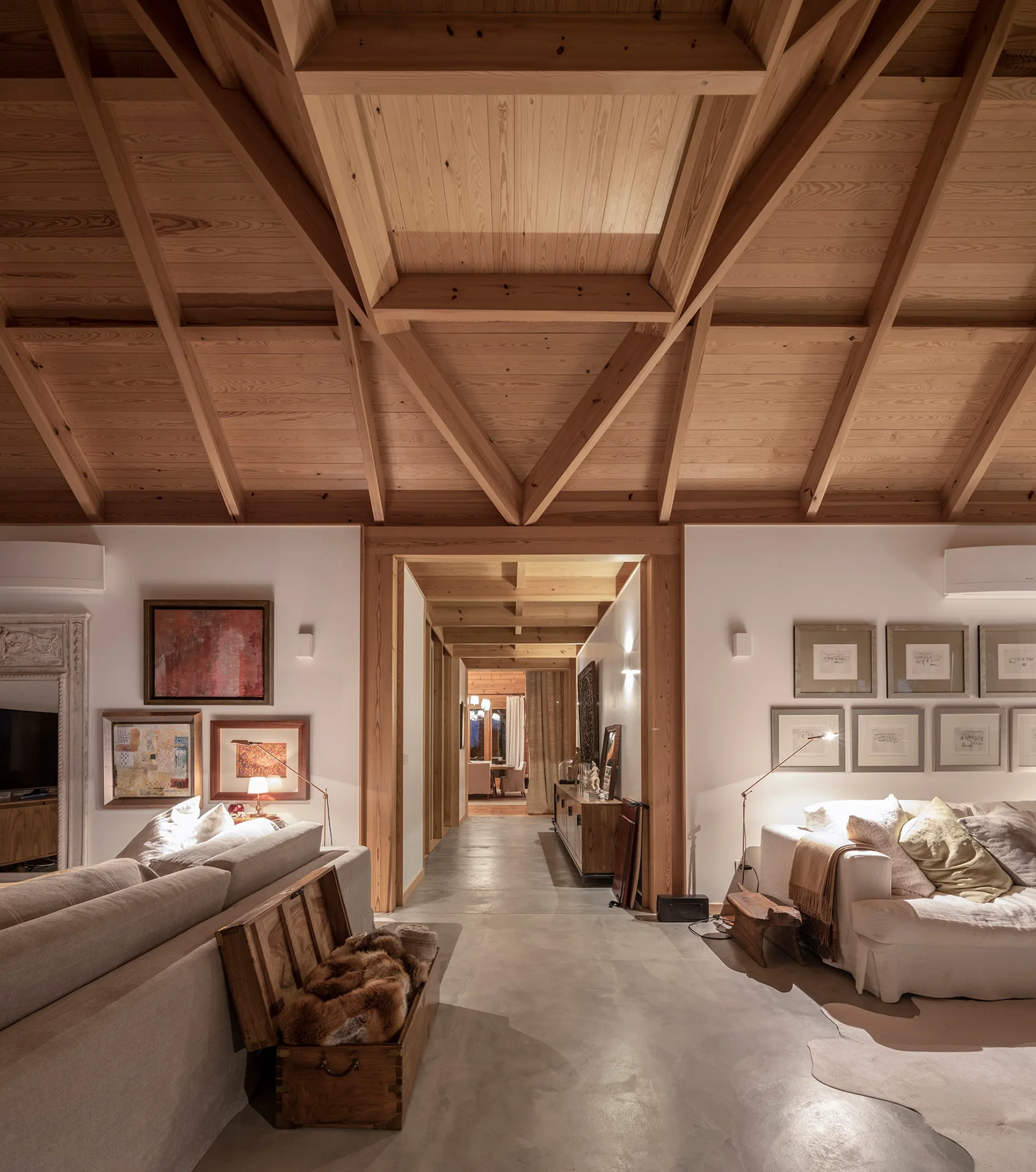 A rustic living room featuring beige sofas, polished concrete floors, and a dramatic vaulted ceiling with exposed wood beams.