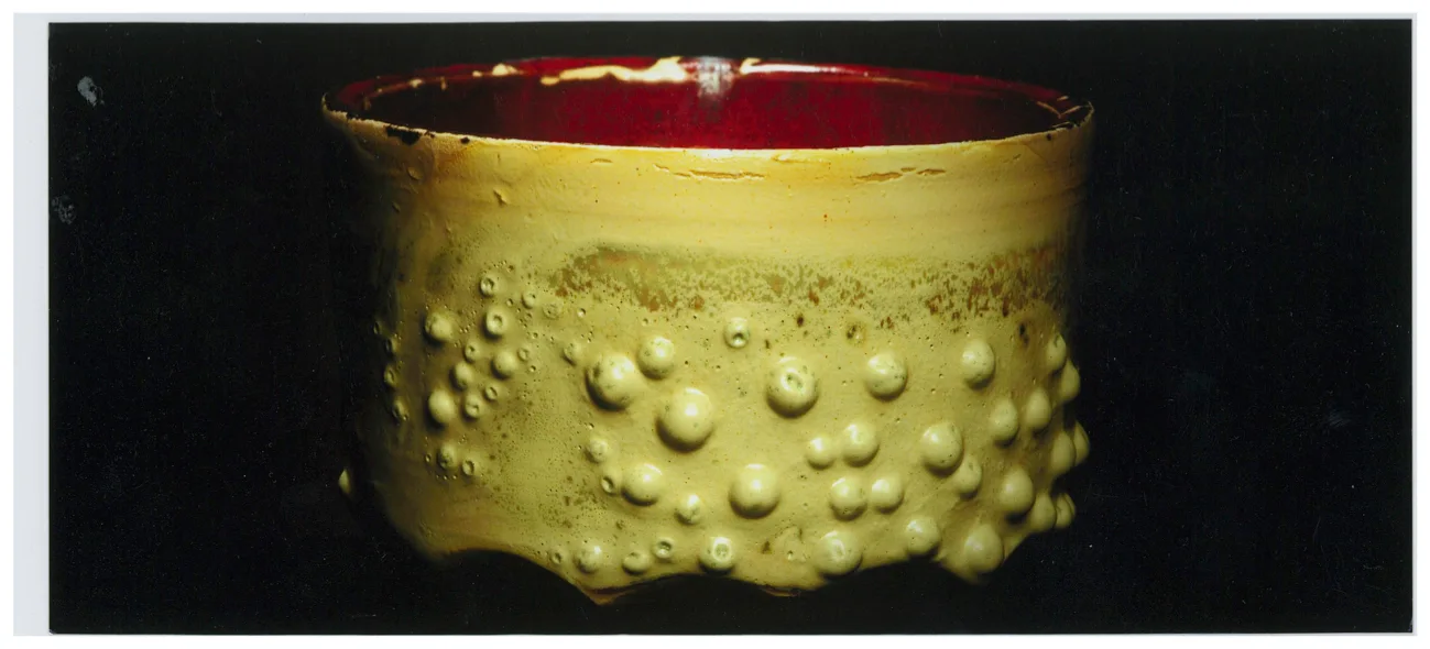 A low yellow ceramic bowl features a raised bubbly texture on the exterior and a smooth red glaze on the interior.