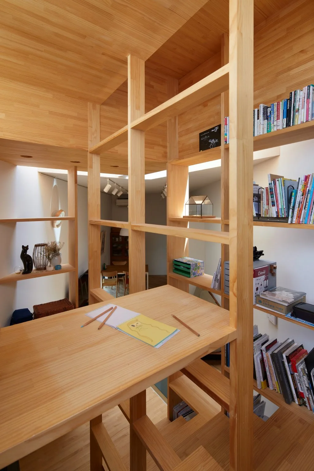 A built-in light wood desk is integrated into a floor-to-ceiling grid shelving unit filled with books and small decor under natural light.