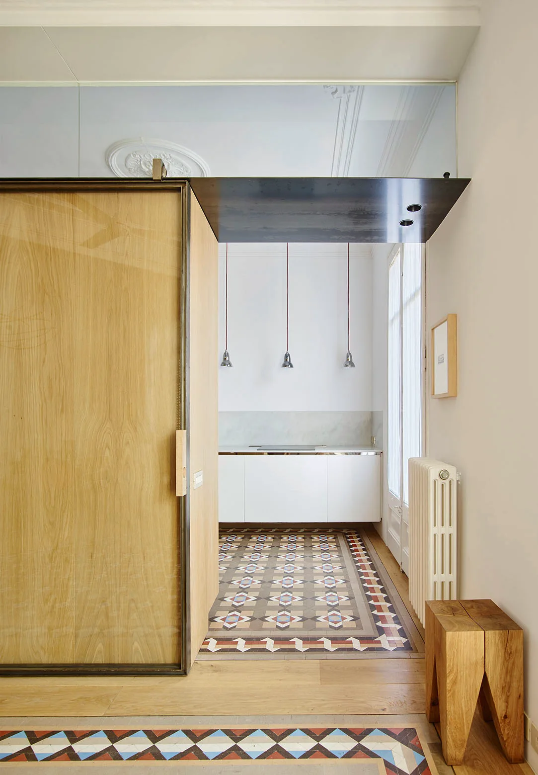 A modern kitchen features white cabinets, three pendant lights, a geometric patterned tile floor, and a large sliding wood door.