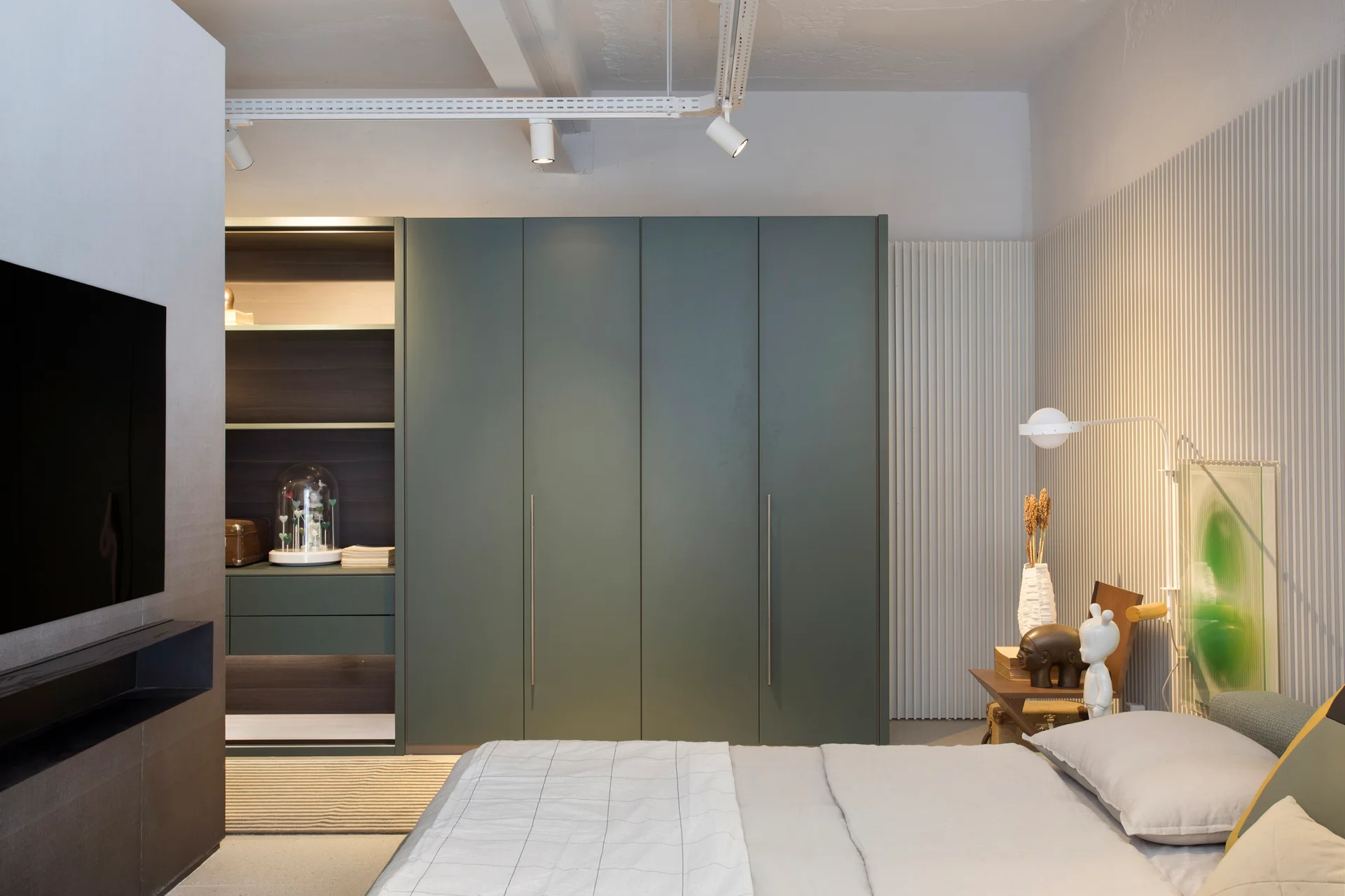 A contemporary bedroom features a large sage green built-in wardrobe, a bed with grey bedding, and a white vertical slatted accent wall.