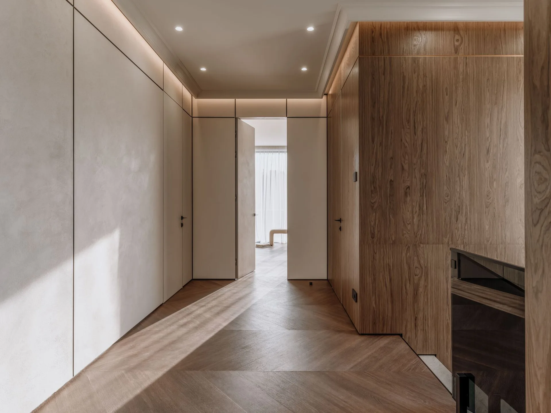 A modern hallway features chevron wood flooring, warm wood paneling, and flush-mount doors integrated seamlessly into the walls.