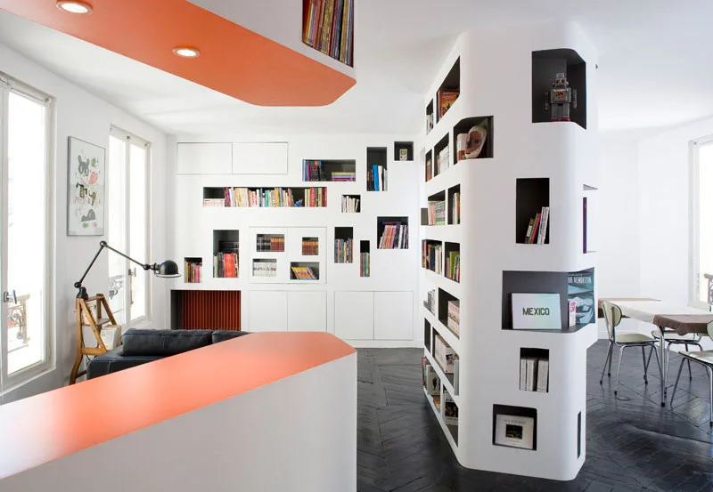 A modern room featuring a sculptural white partition bookshelf, orange ceiling panel, and dark herringbone wood floors.