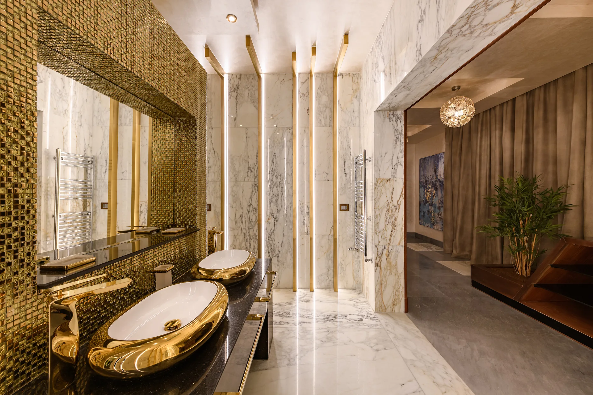 A modern bathroom features a dark vanity with two gold vessel sinks, a marble-paneled wall with vertical gold strip lighting, and a large mirror.
