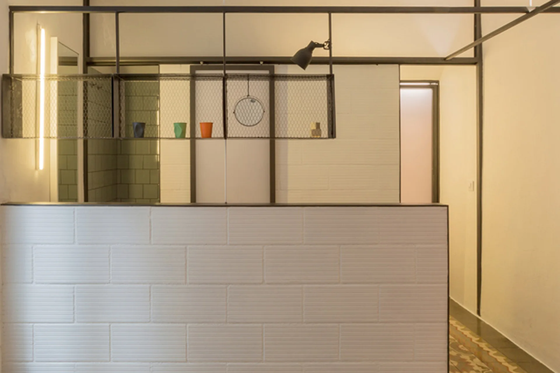 A low white brick partition wall sits below a suspended black metal wire mesh shelving unit.
