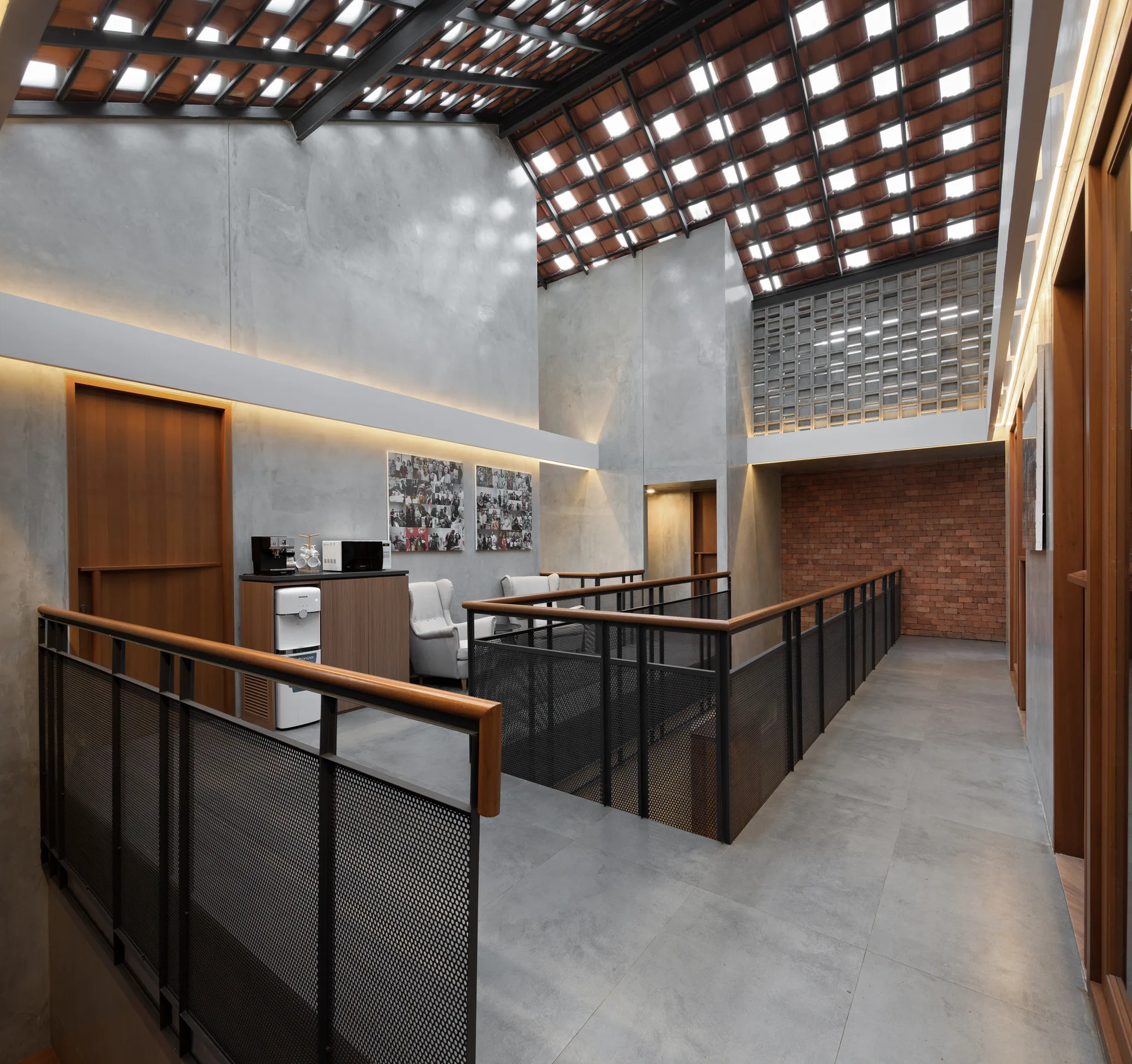 An industrial interior landing features smooth concrete walls, a black mesh railing with wood trim, and a high terracotta tiled skylight roof.