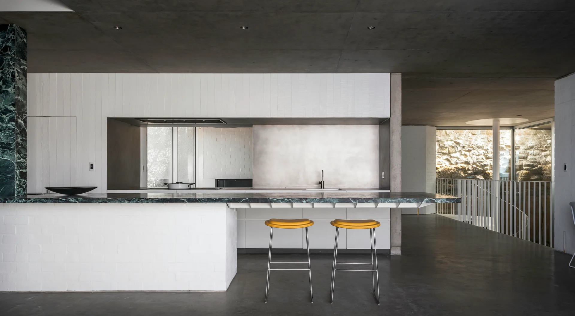 A modern kitchen featuring a white brick island with a green marble countertop, two yellow bar stools, and a dark grey ceiling.