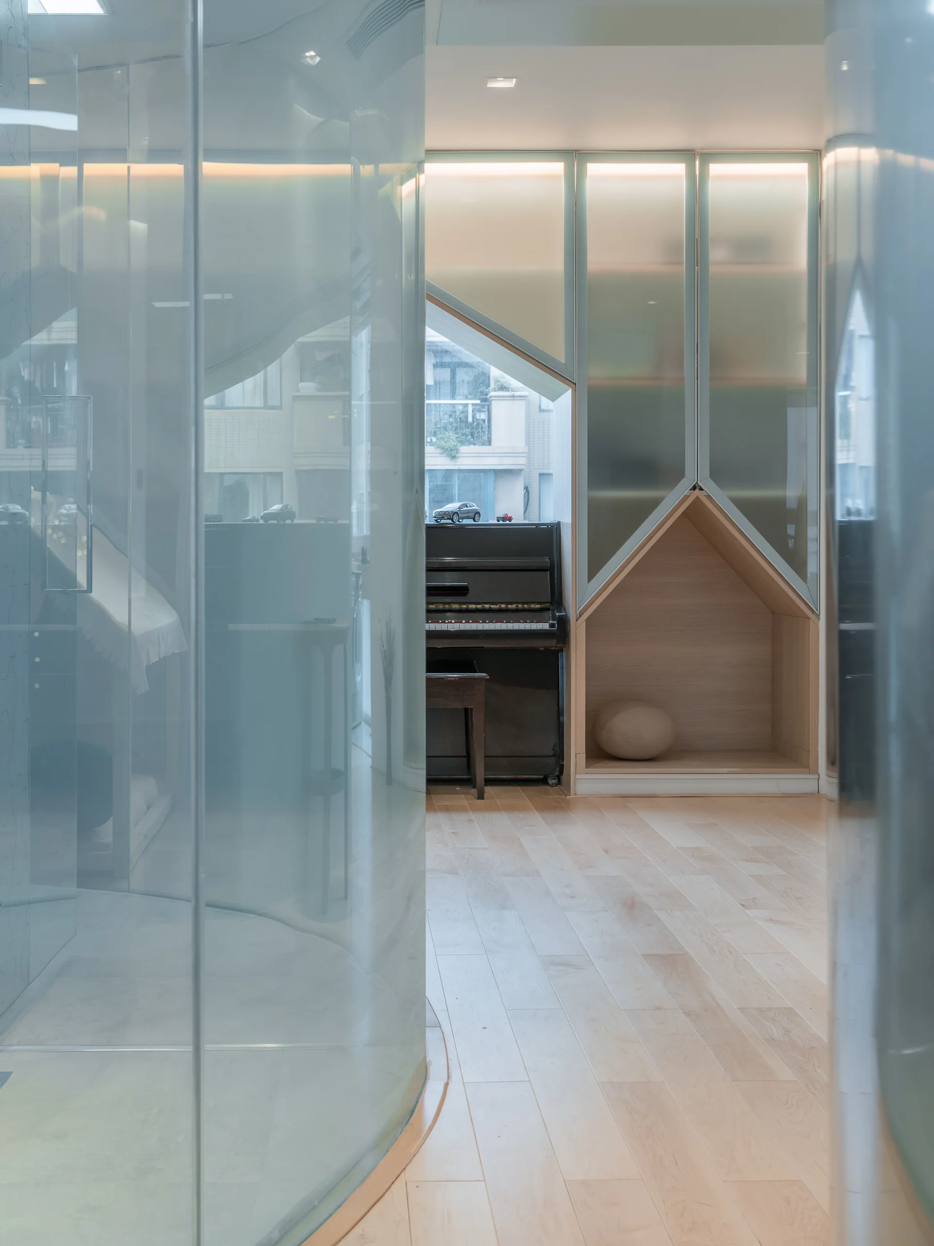 A modern room featuring light wood floors, an upright black piano by a window, and custom built-in cabinets with a house-shaped niche.
