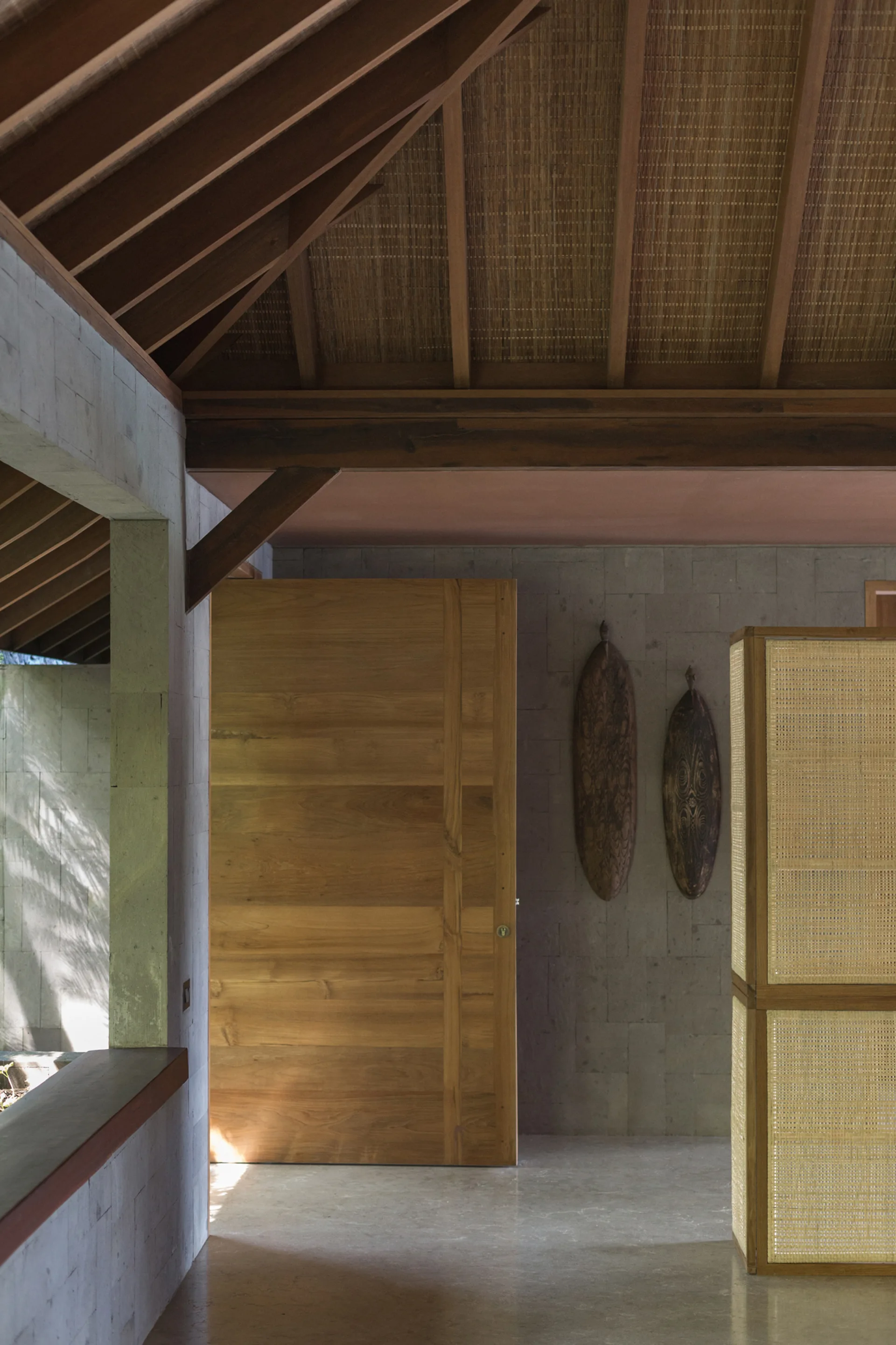An entryway features a large wooden pivot door, grey stone block walls, and an exposed timber ceiling with woven panels.