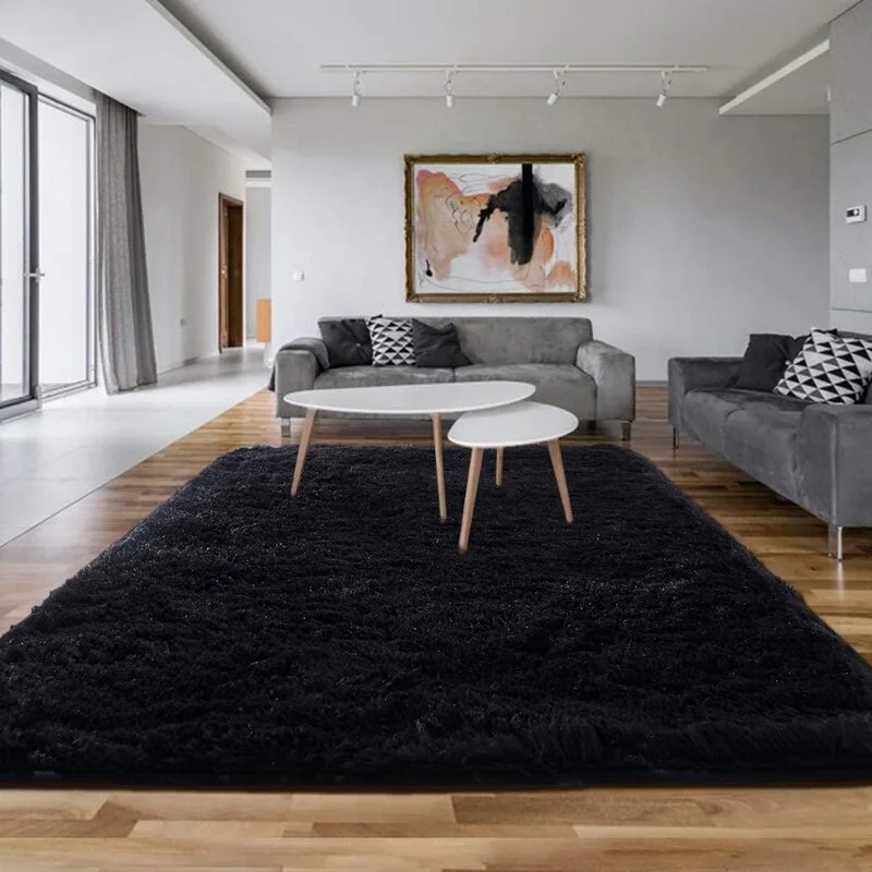 A contemporary living room featuring two gray sofas, nested white coffee tables, and a large black shag rug on wood plank flooring.