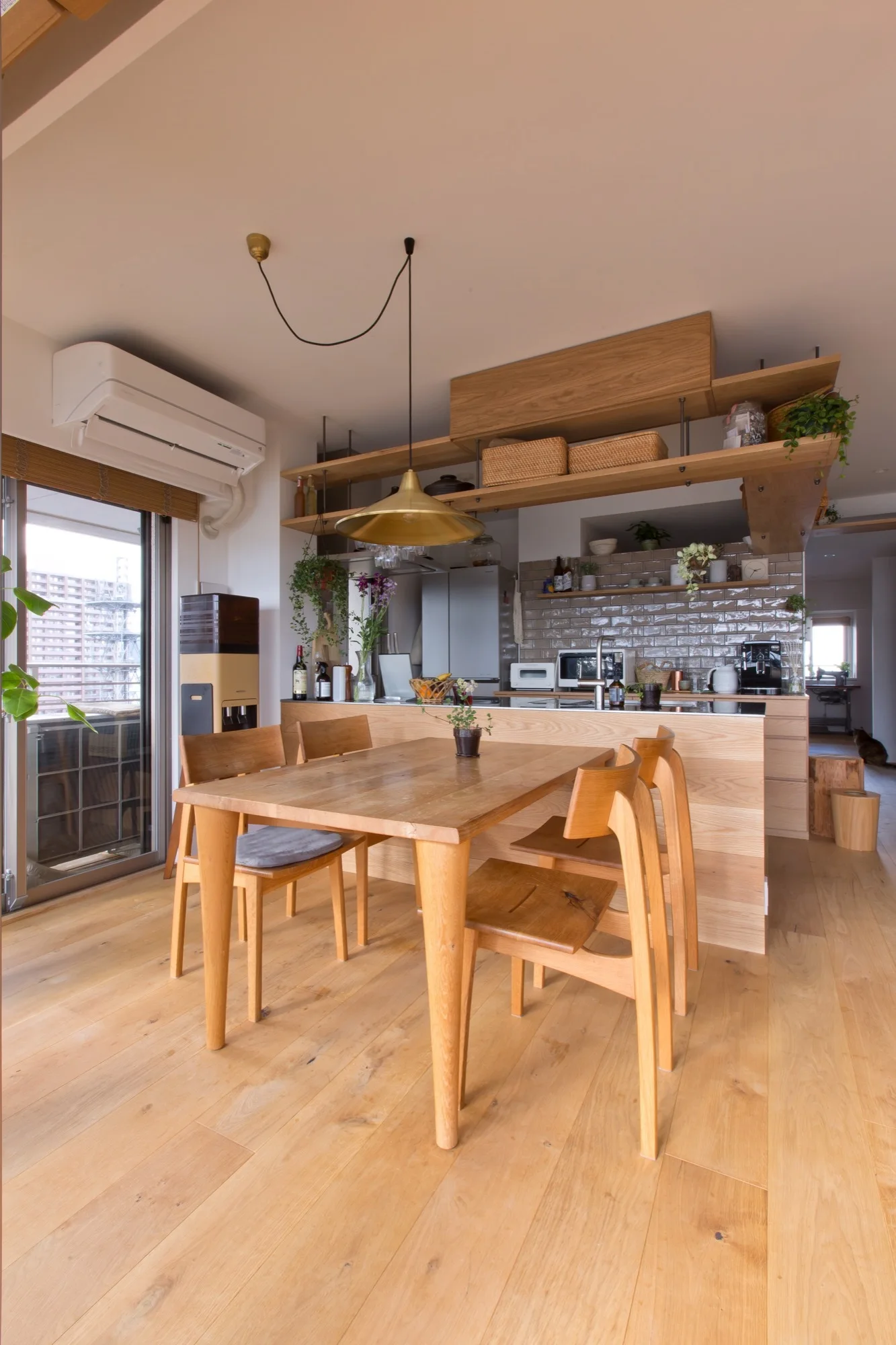 An open-plan kitchen features a light wood dining set, a wood-paneled island, and open shelves decorated with wicker baskets.