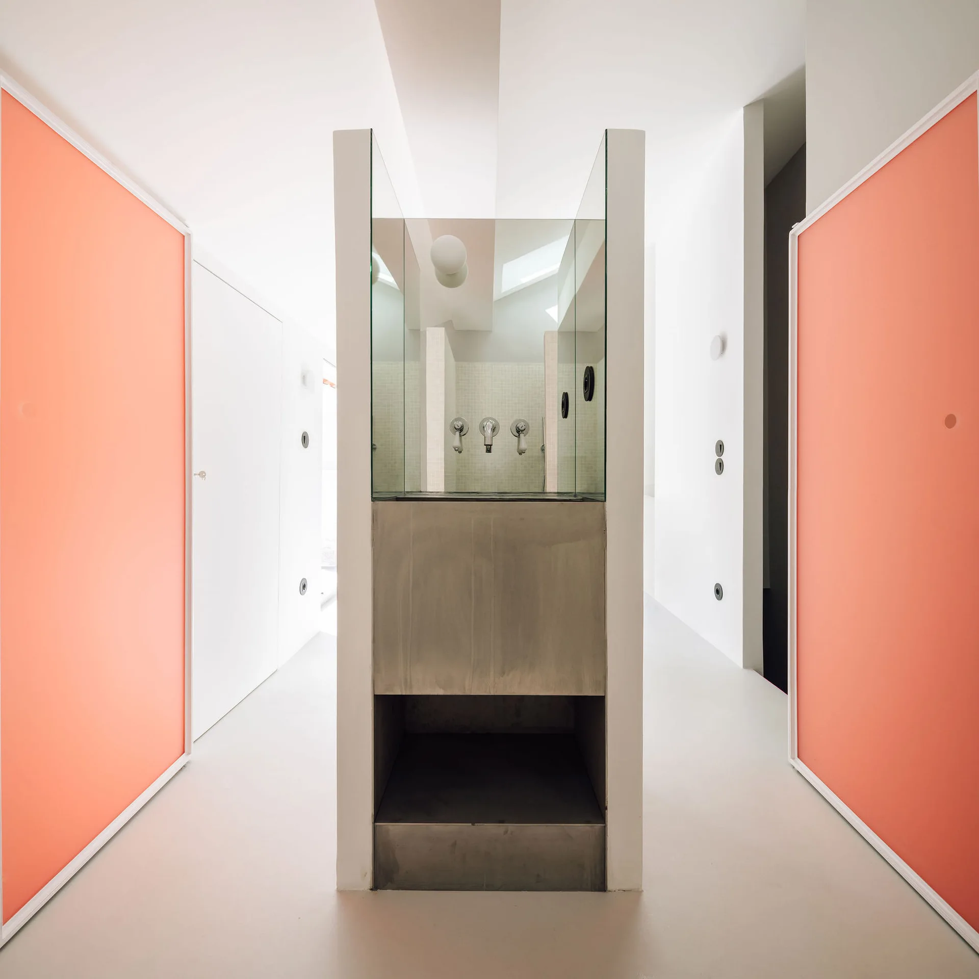 A minimalist bathroom features a central metal and glass shower enclosure flanked by bright salmon-colored panels and white walls.
