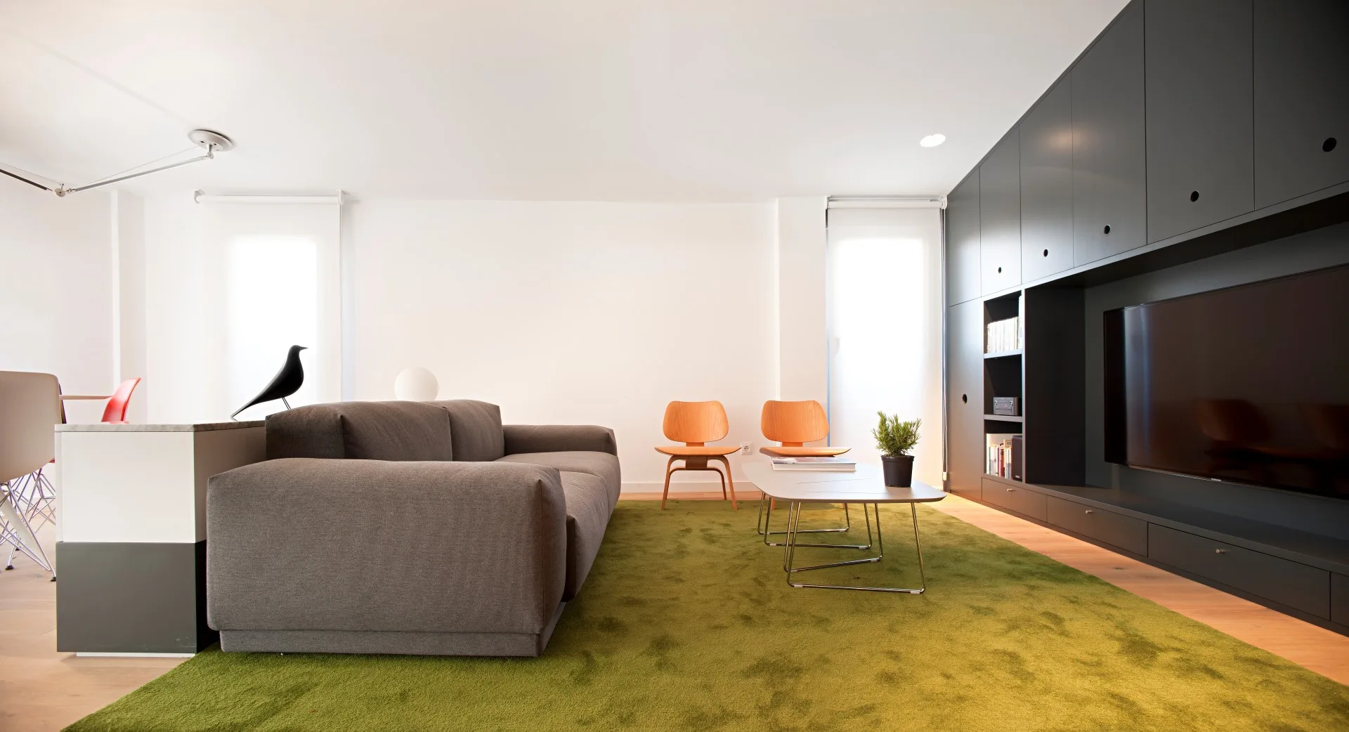 A modern living room with a grey fabric sofa on a green rug and a large charcoal grey built-in media storage unit.