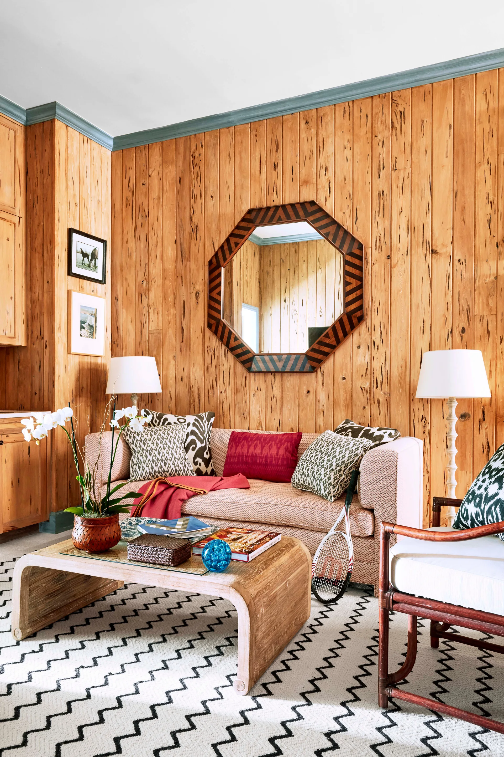 A living room features vertical wood plank walls, a beige upholstered sofa, a curved wood coffee table, and an octagonal mirror.