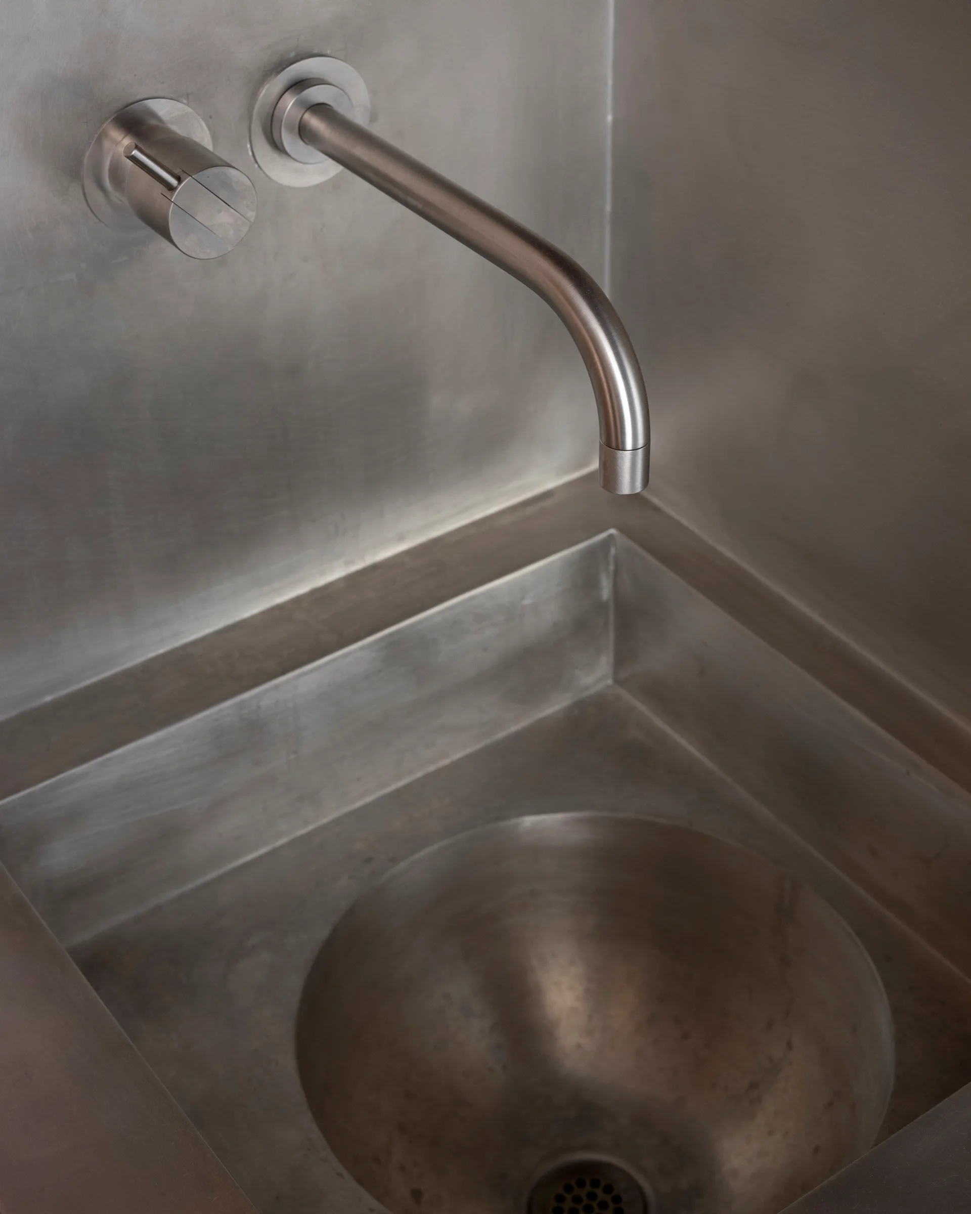 A close-up of an integrated brushed metal sink basin with a matching wall-mounted faucet and cylindrical handle.