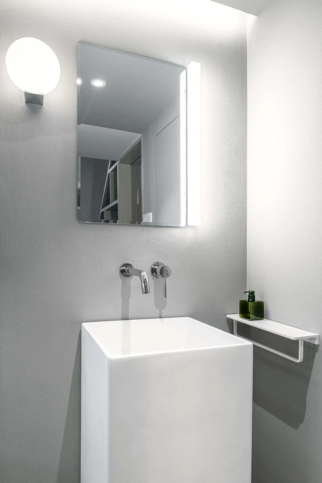 A modern powder room featuring a white square pedestal sink, a chrome wall-mounted faucet, a rectangular mirror, and a globe wall sconce against gray walls.