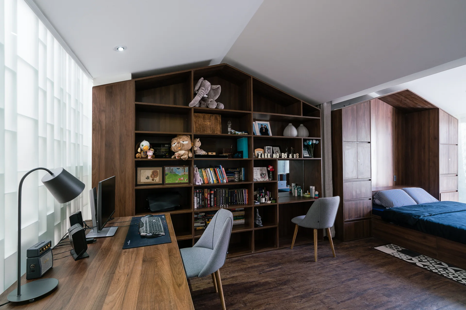 A modern bedroom featuring custom dark wood built-in shelves shaped like a house, an integrated desk, two gray chairs, and a matching platform bed.