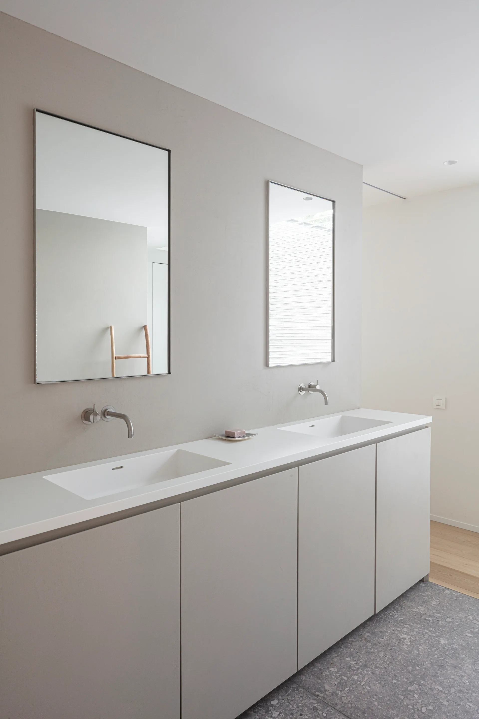 A minimalist bathroom features a long greige vanity cabinet with integrated sinks, wall-mounted silver faucets, and two simple rectangular mirrors.