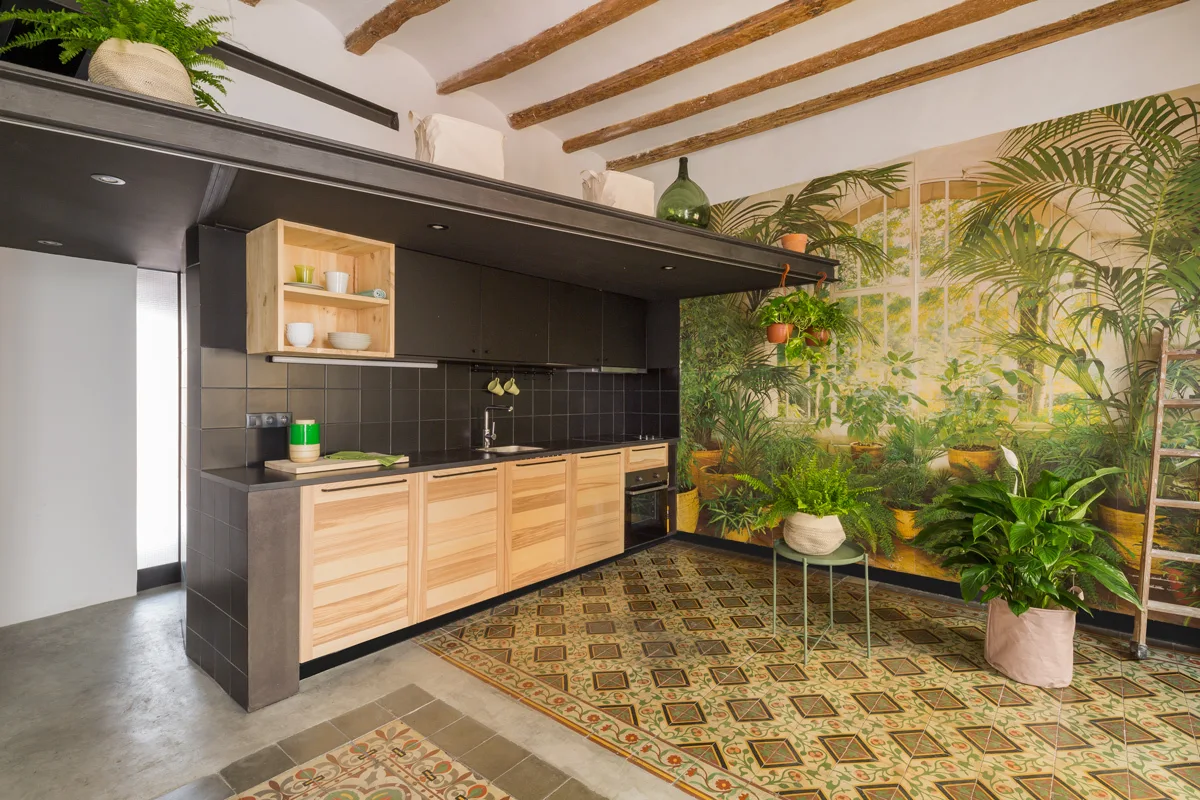 A modern kitchen features black cabinetry, a botanical wall mural, exposed ceiling beams, and patterned floor tiles.