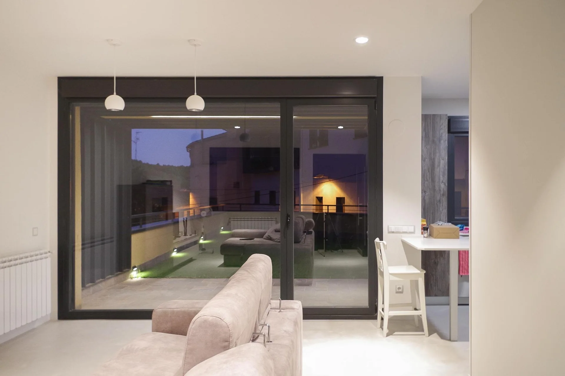 A beige sofa sits in a minimalist living room featuring a large sliding glass door that leads to an outdoor balcony.