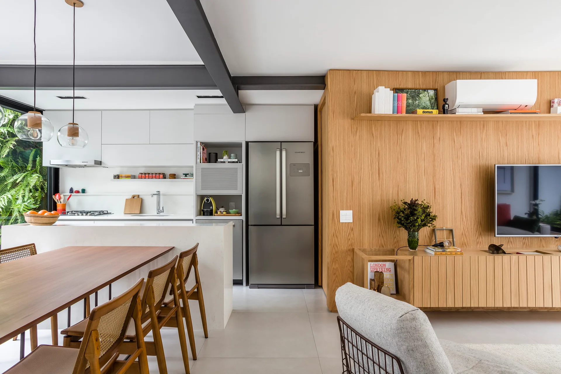 An open-concept kitchen and living space features a white kitchen island, a wooden dining table with cane chairs, and a light oak wood paneled wall.