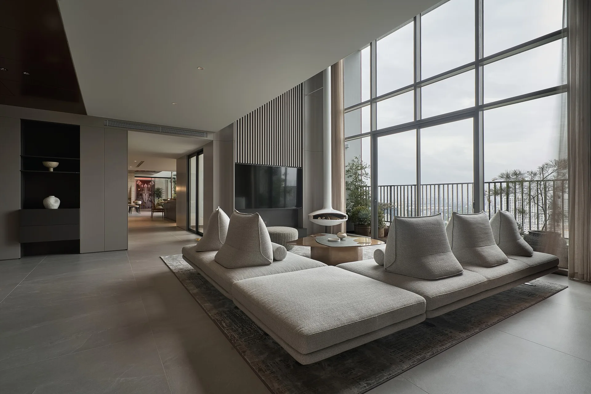 A minimalist living room features a low-profile grey modular sofa, a suspended white fireplace, and floor-to-ceiling windows opening to a balcony.