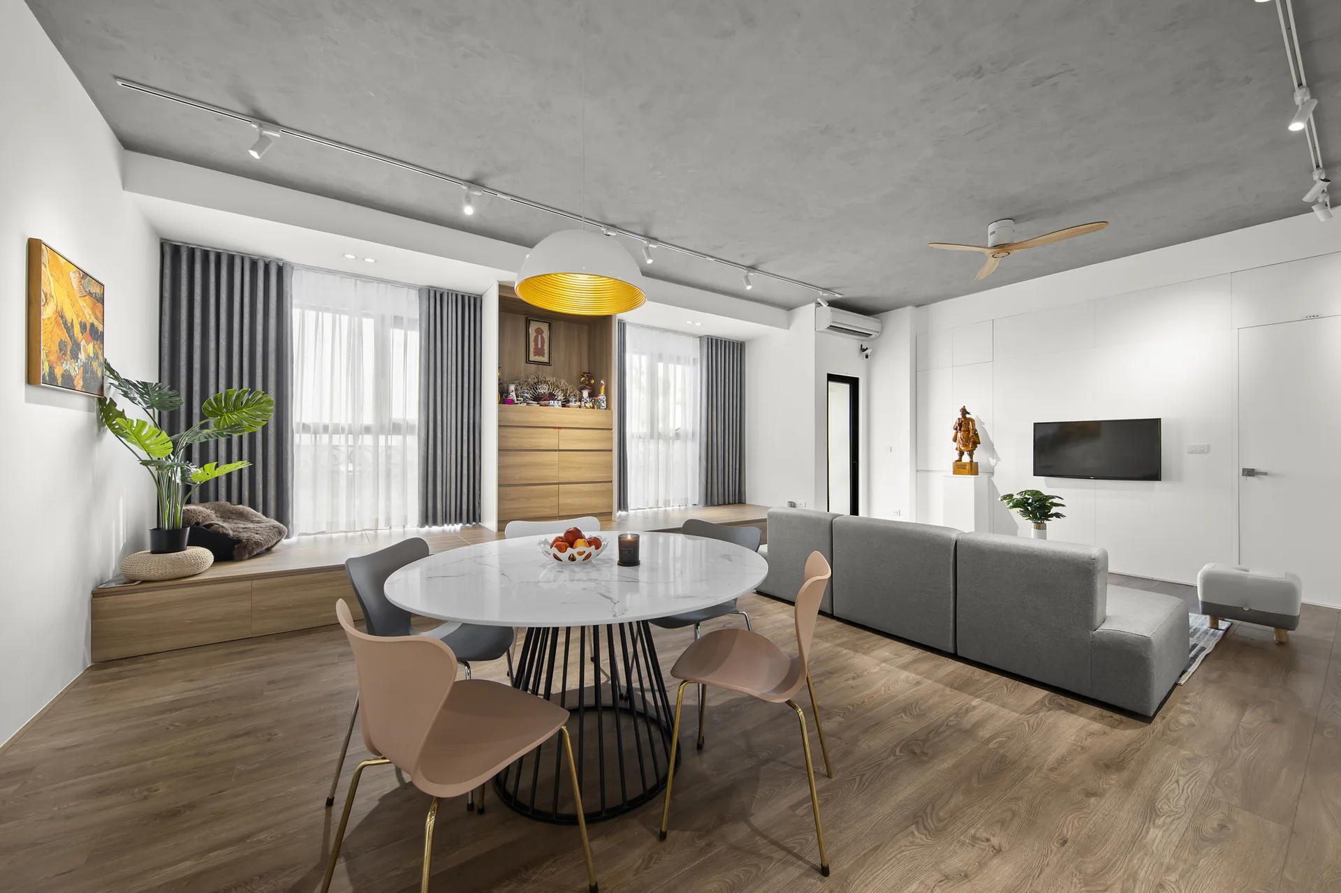 A modern open-concept living and dining room features a round marble table, grey sectional sofa, wood flooring, and a textured concrete ceiling.