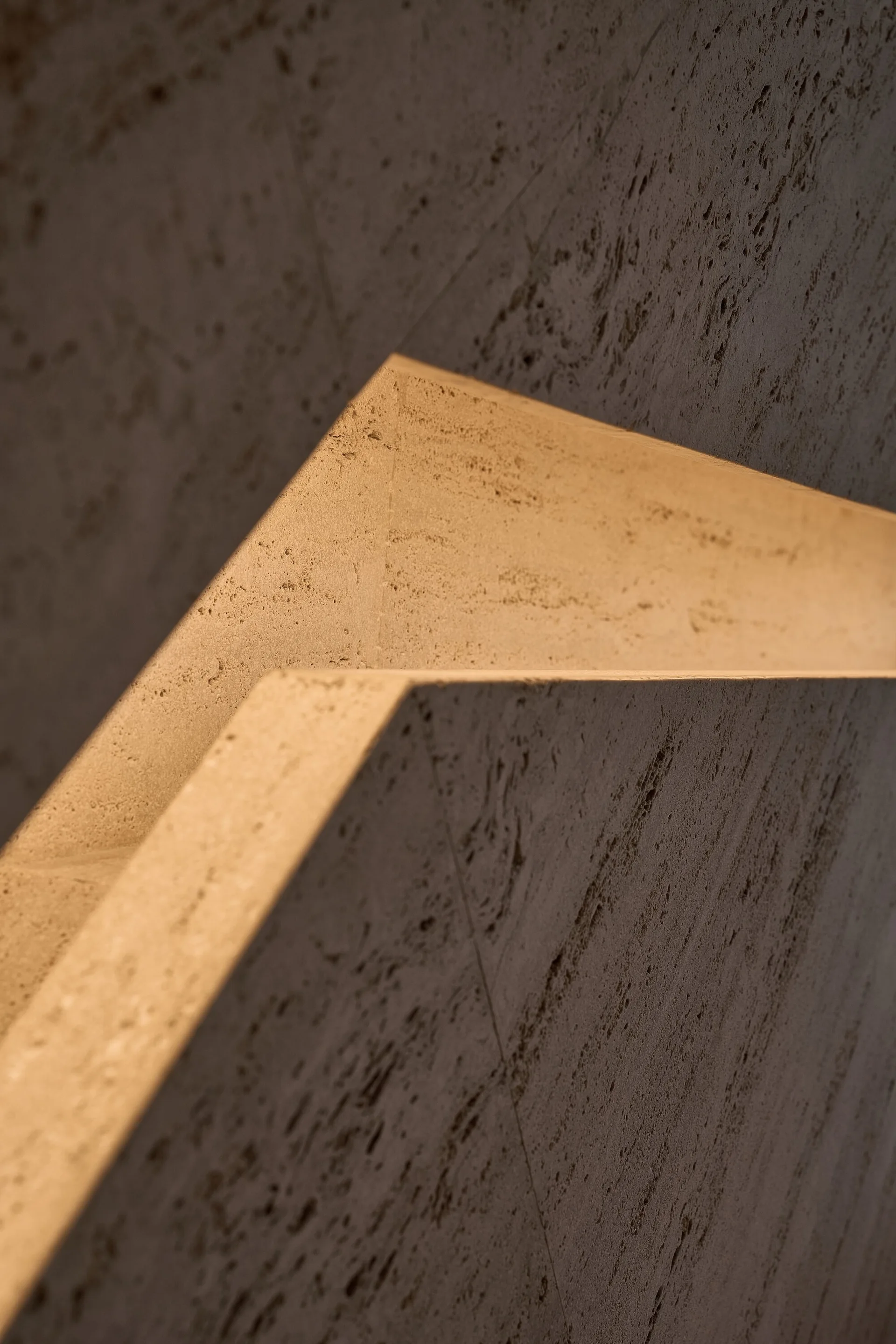 Close-up of textured grey stone wall panels with sharp geometric angles and integrated warm cove lighting glowing along the recessed edge.