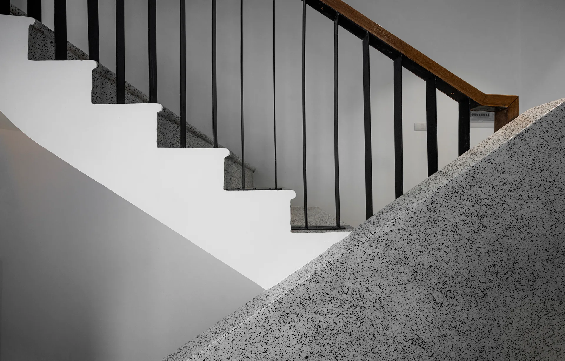 A modern staircase features speckled grey terrazzo treads, smooth white risers, and a black metal railing with a natural wood handrail.