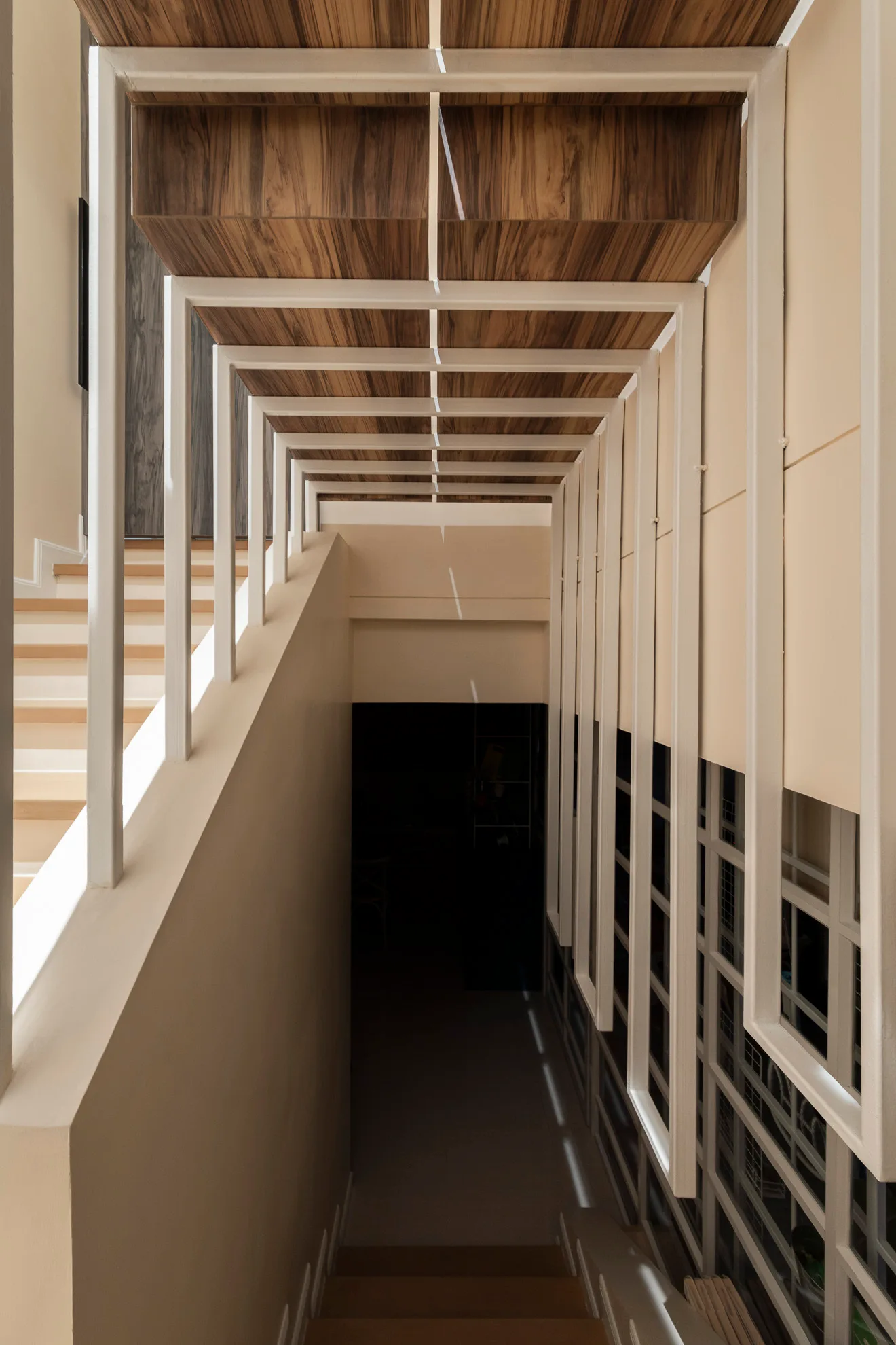 A modern staircase features a white metal geometric railing that extends overhead into wood-paneled ceiling rafters alongside beige walls.