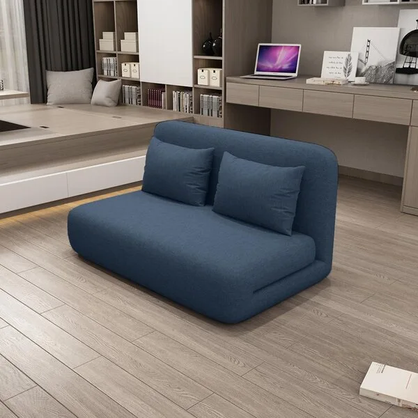 A low-profile blue fabric floor sofa sits on light wood flooring in a minimalist room with built-in wooden shelving and a desk.