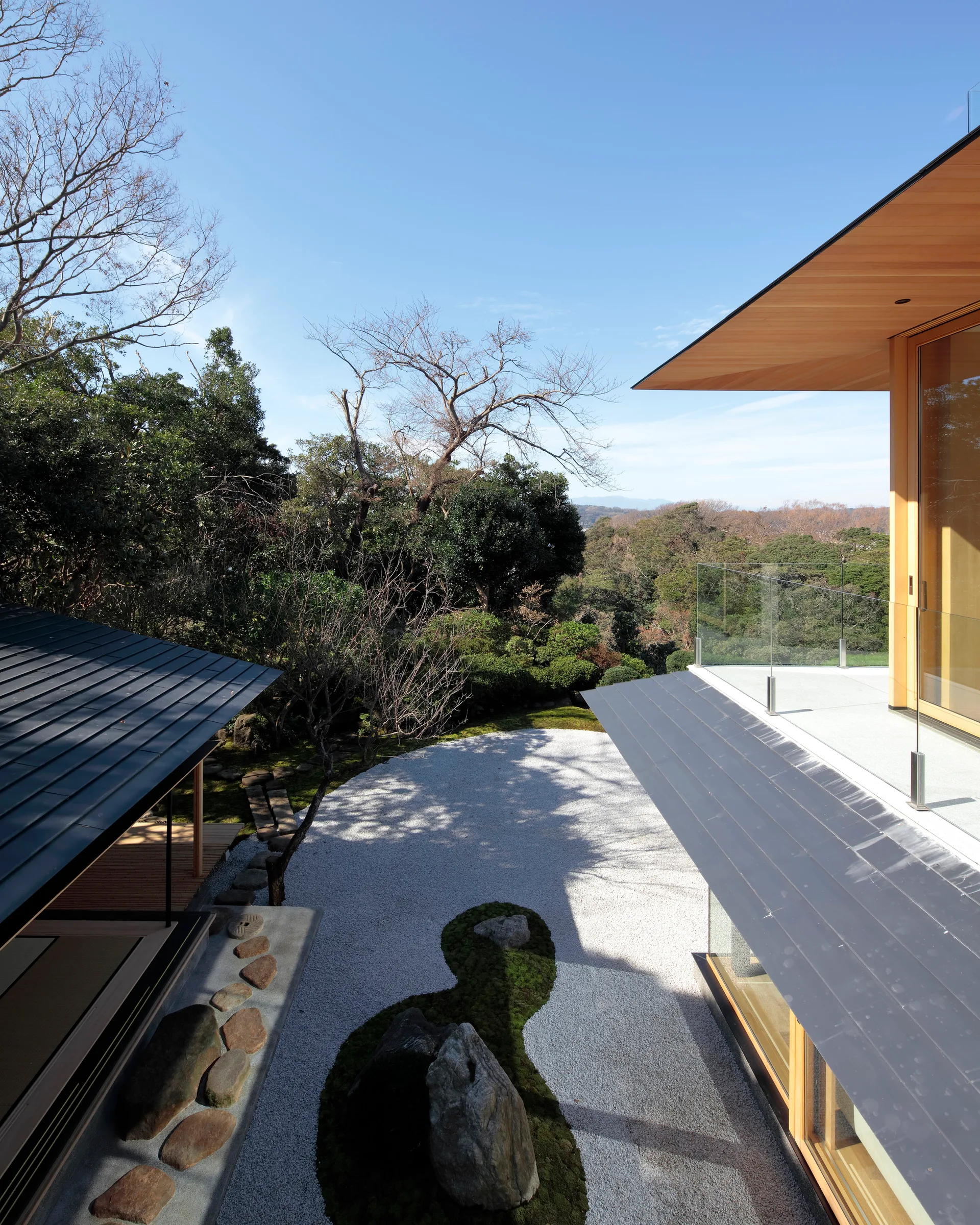 An overhead view of a modern residence with wood eaves overlooking a gravel garden with stepping stones and landscape rocks.
