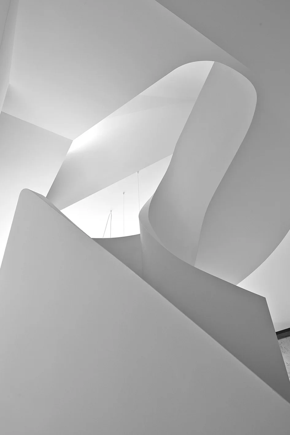 A minimalist white staircase features a continuous curved balustrade and a smooth matte plaster finish under soft light.
