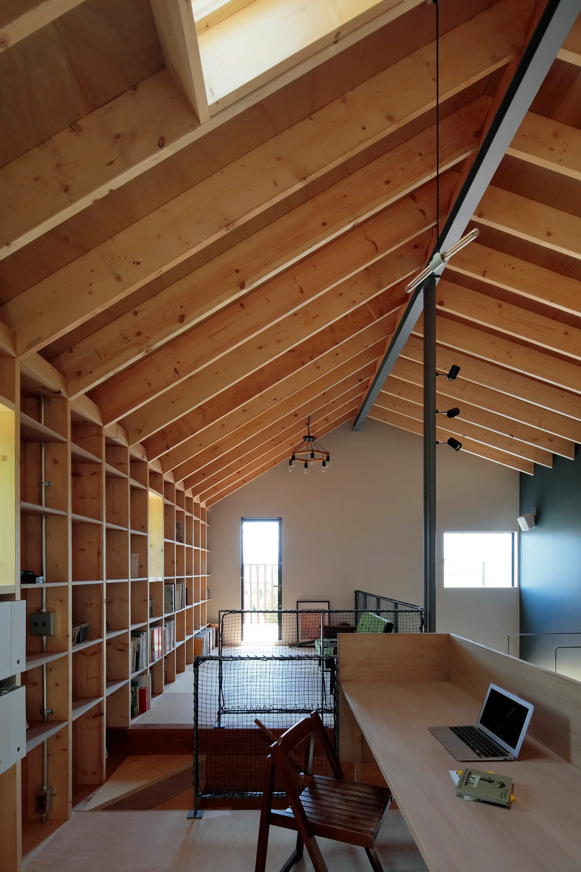 A lofted home office features a vaulted wooden ceiling, a large built-in grid bookshelf wall, and a wood desk with a laptop.