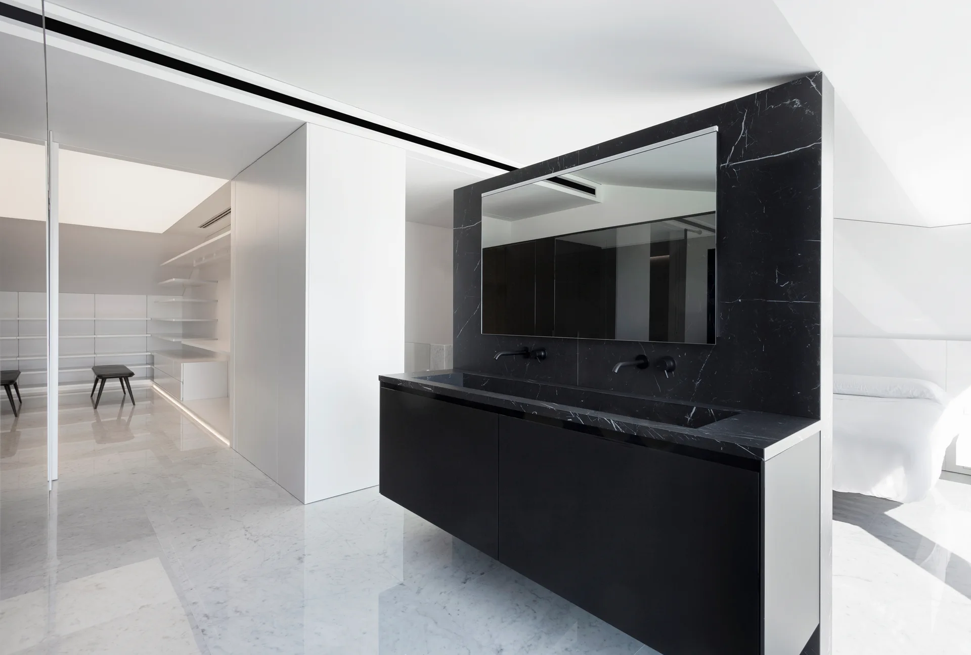 A modern bathroom features a floating black marble vanity with an integrated sink below a frameless mirror with polished marble floors.