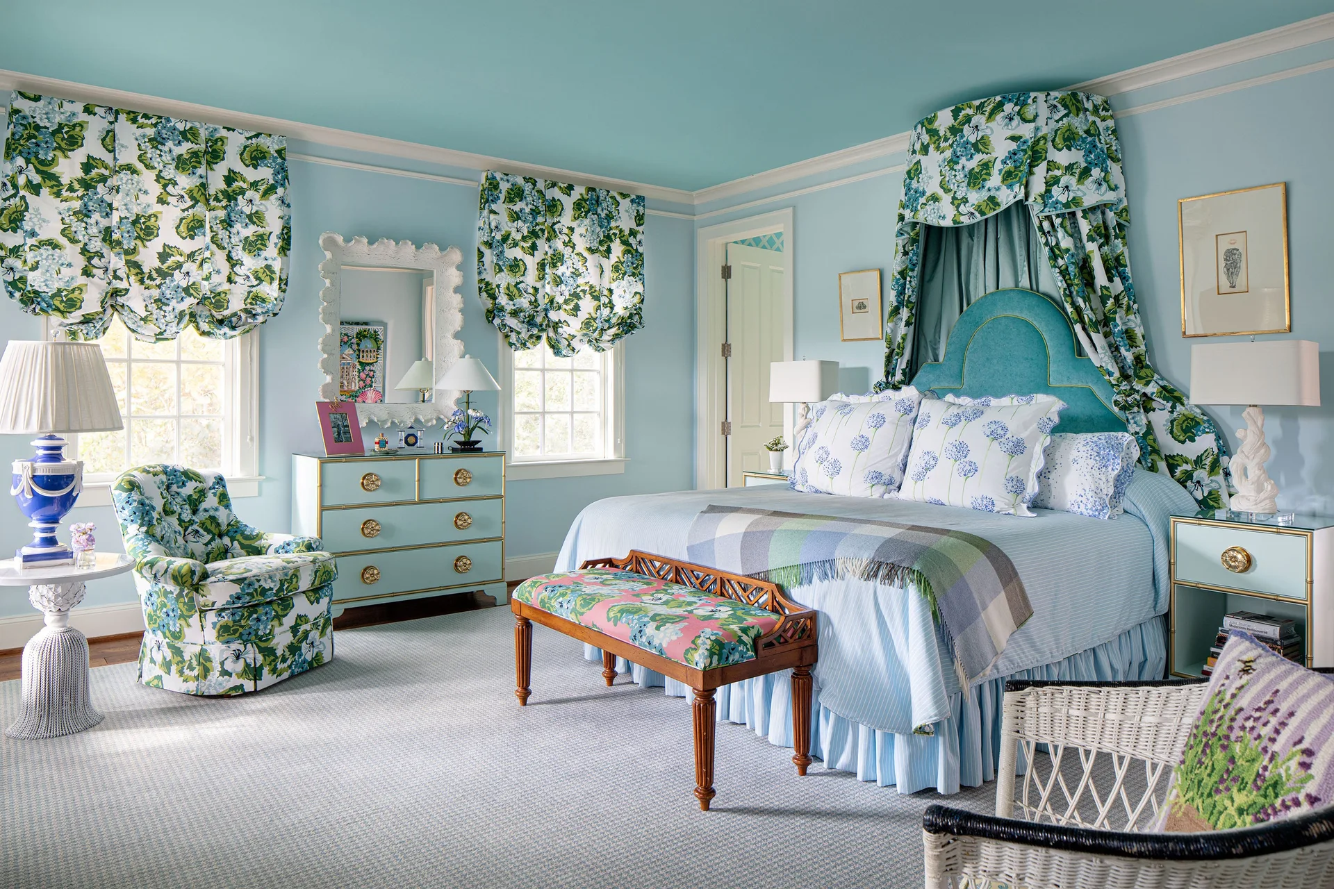 A light blue bedroom features a canopy bed with floral drapery, matching blue dressers, a floral armchair, and a patterned carpet.