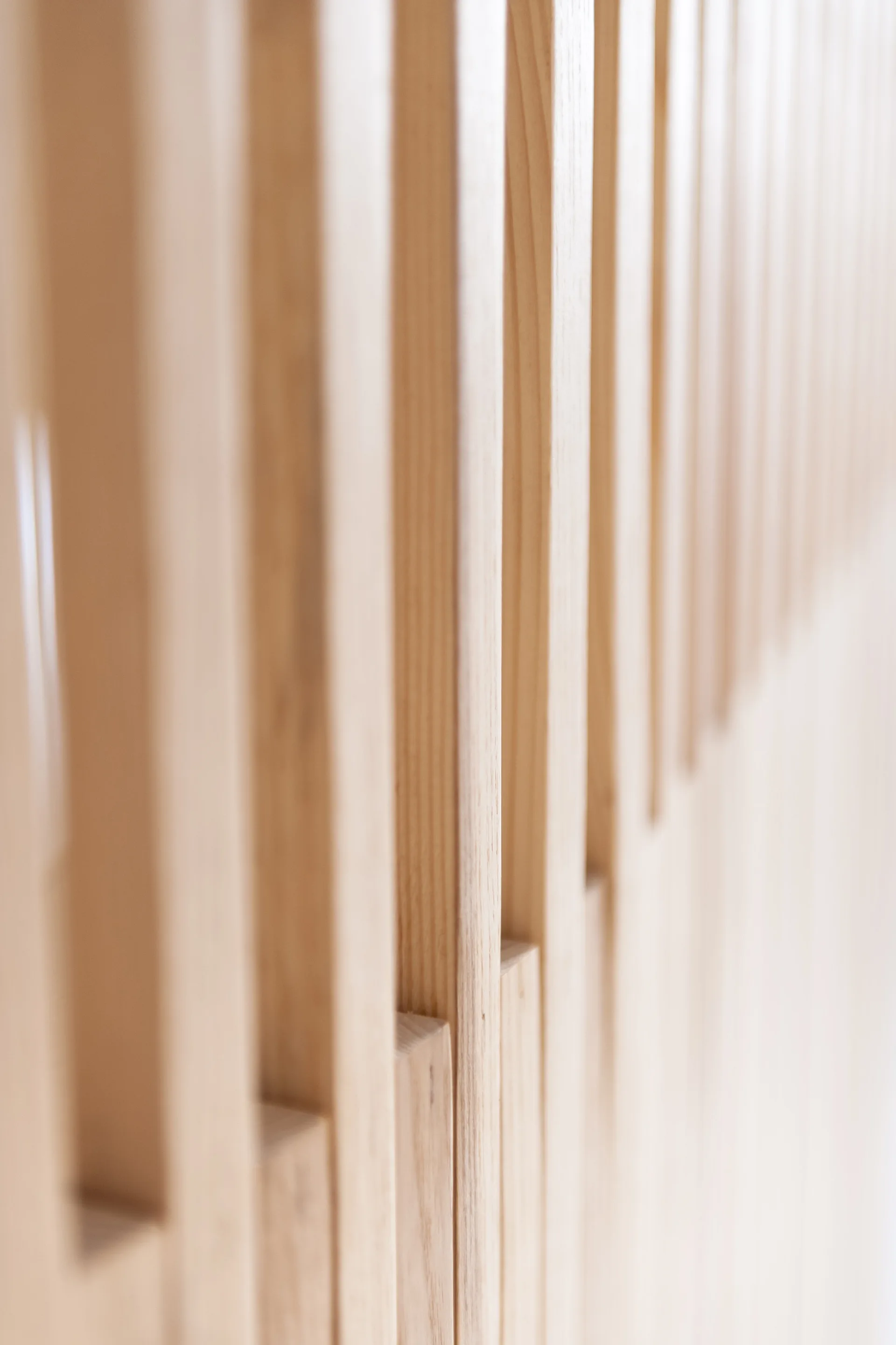 A close-up view of parallel, vertical light wood slats with natural grain on an architectural wall panel.
