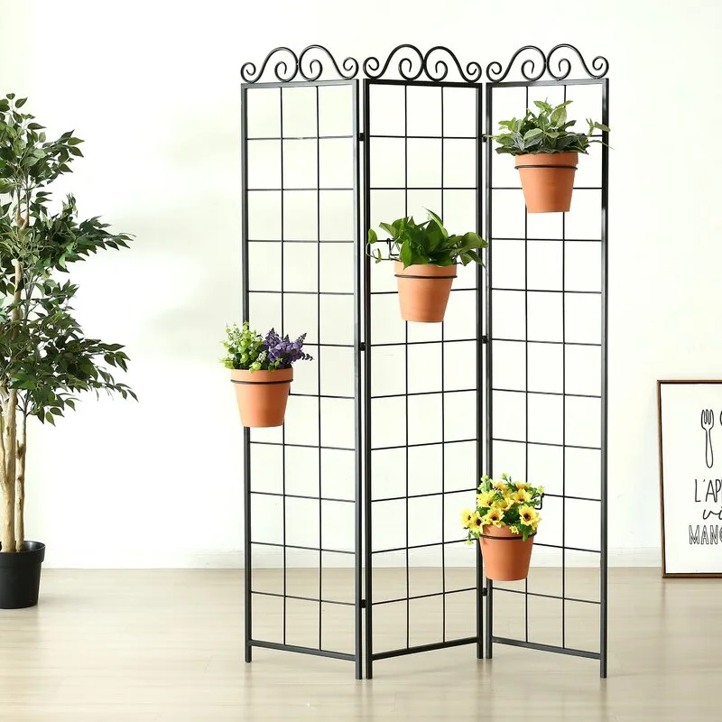 A three-panel black metal grid folding screen with scrollwork details holds four terracotta flower pots against a white wall.