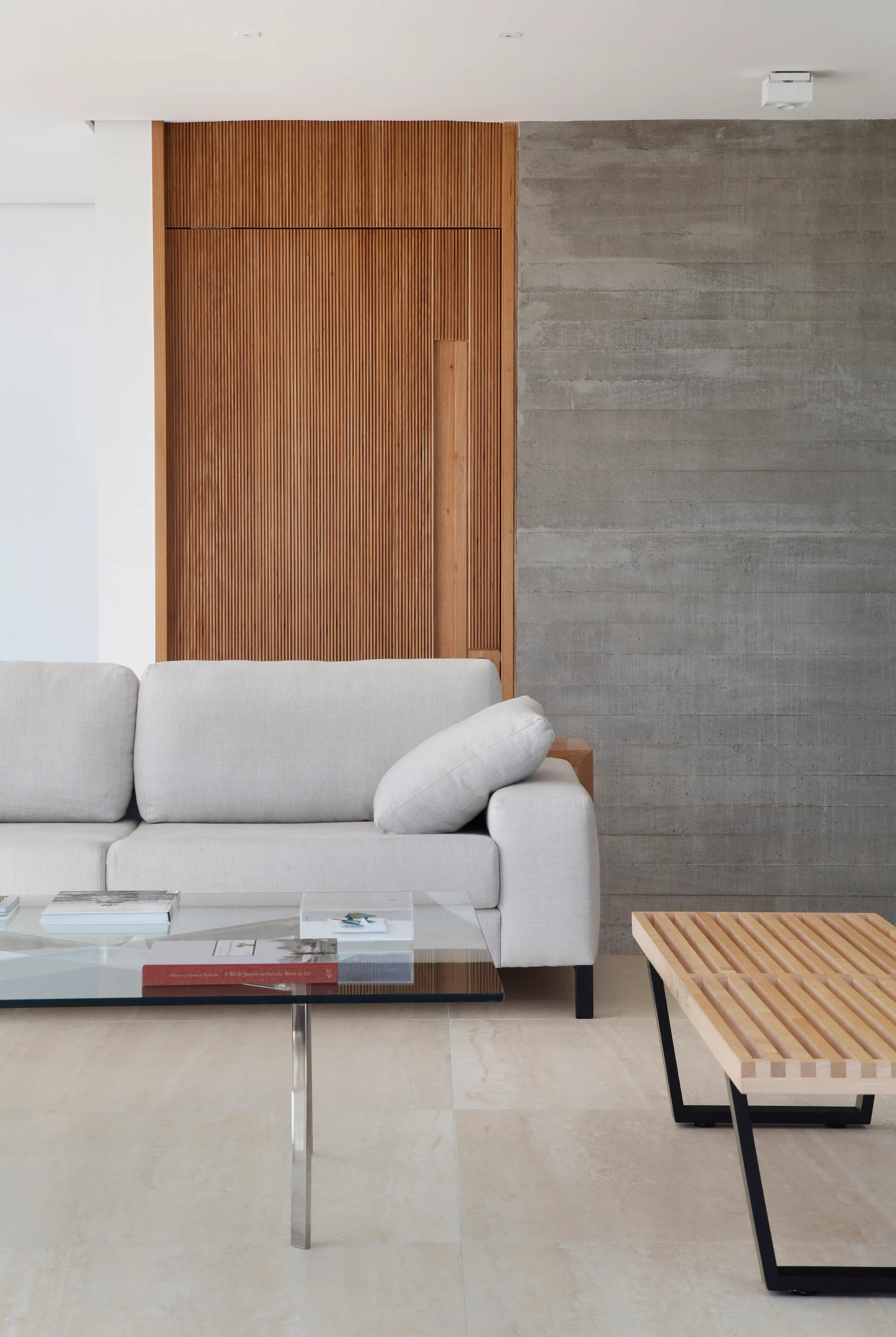 A light gray sofa sits before a feature wall split between vertical wood slats and exposed board-formed concrete in a minimalist living room.