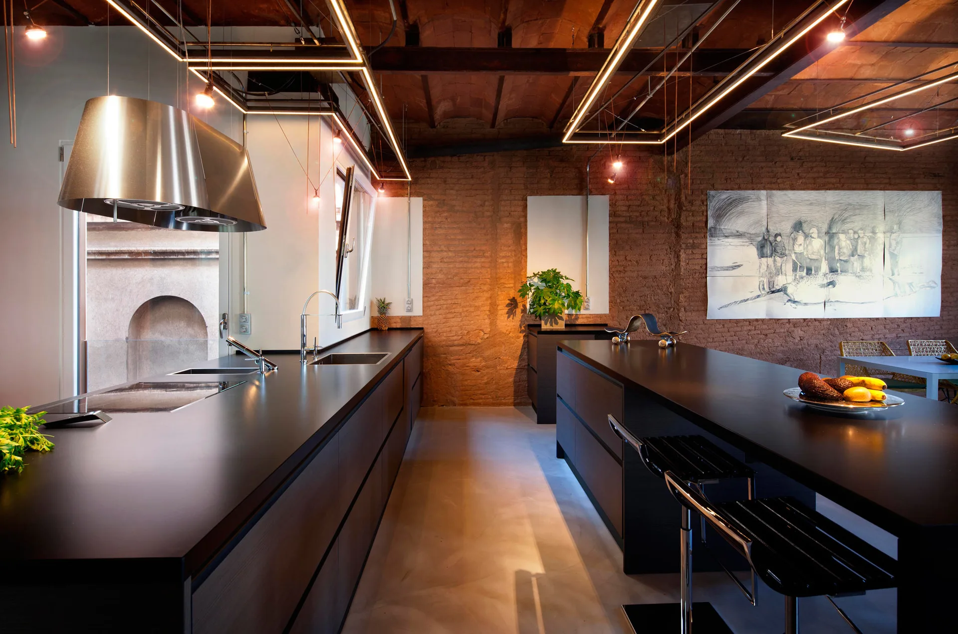 A contemporary industrial kitchen features a dark charcoal island, exposed brick walls, wooden ceiling beams, and suspended geometric linear light fixtures.
