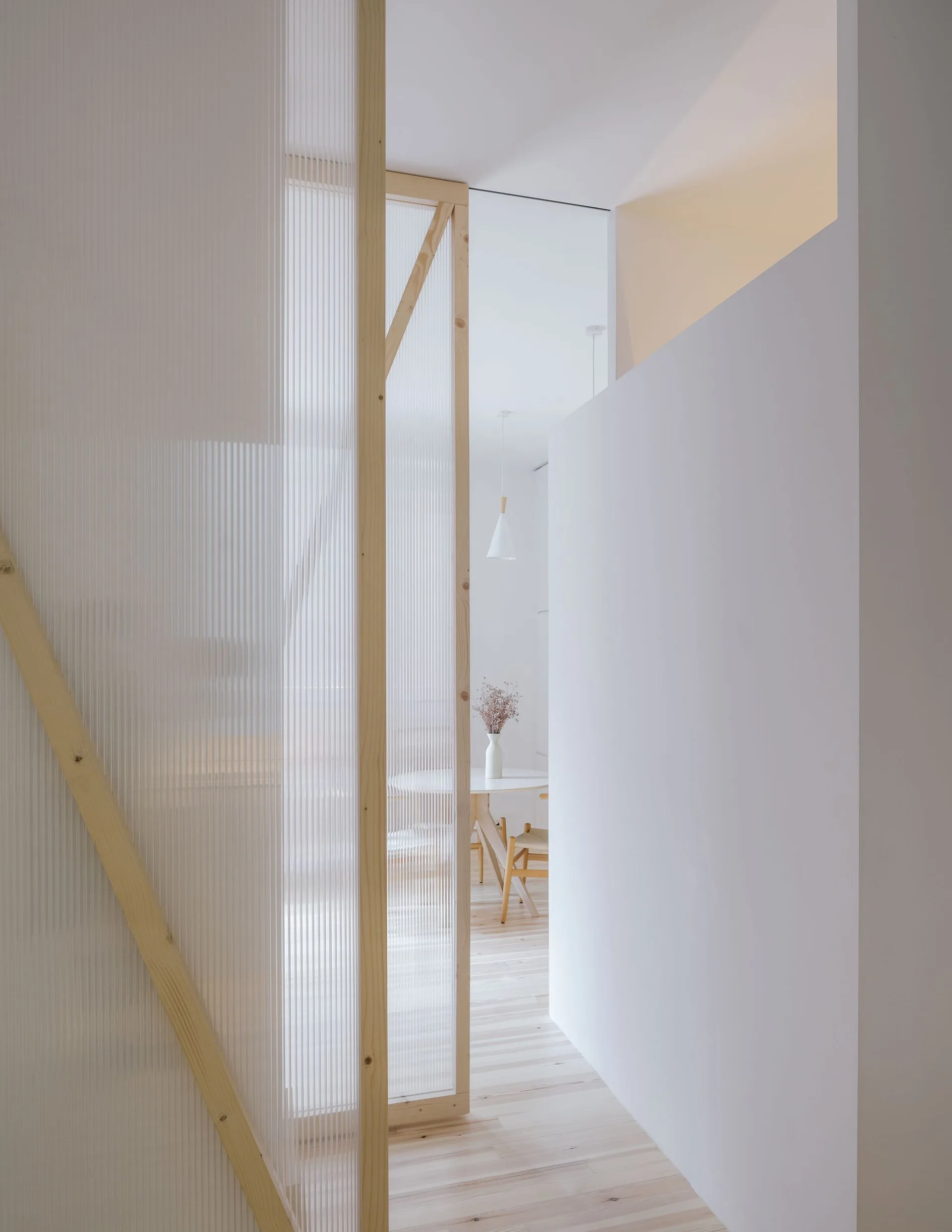 A minimalist interior featuring a fluted glass room divider with a light wood frame looking toward a dining table and chairs.
