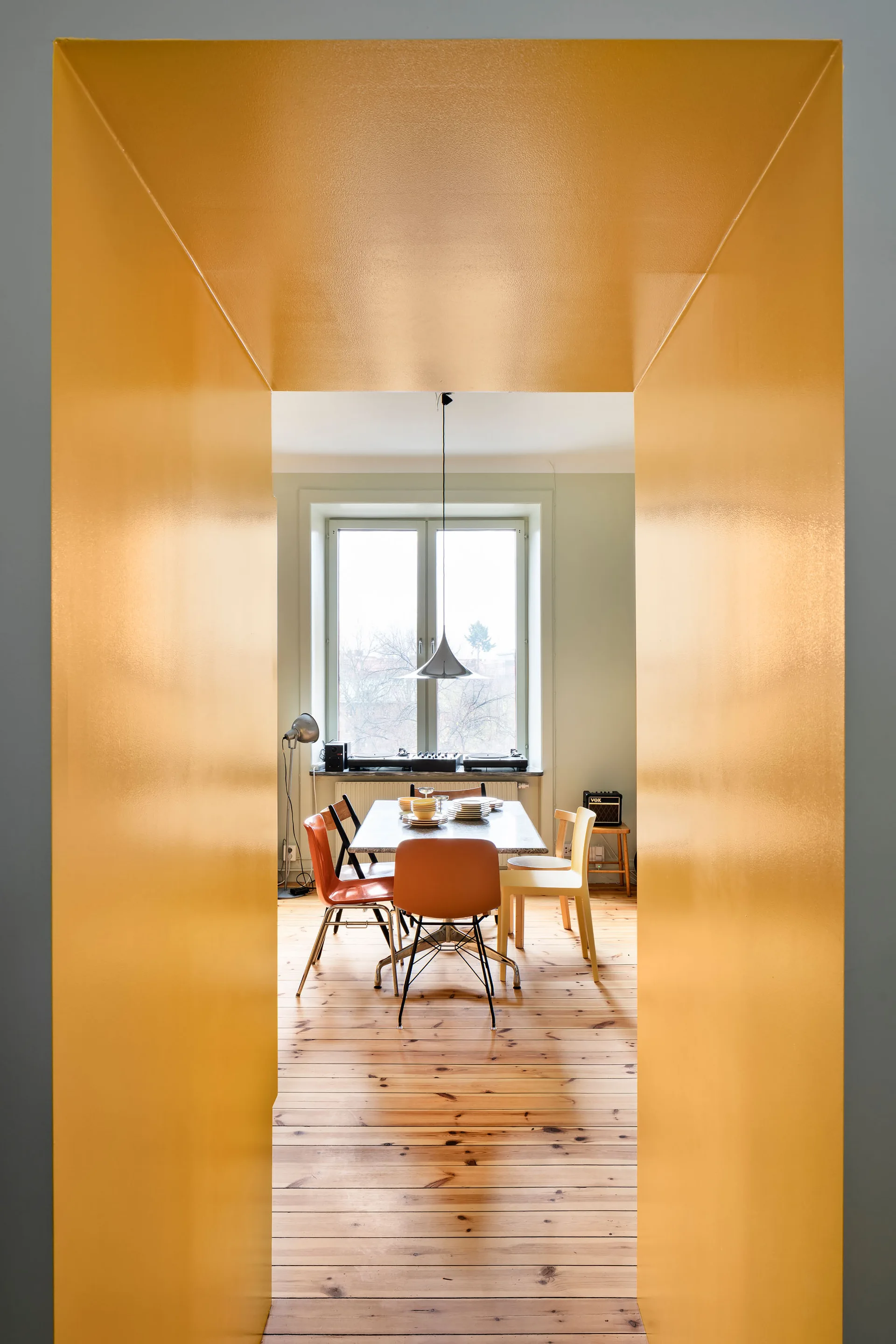 A dining room with wood floors and mismatched chairs seen through a thick, glossy yellow doorway transition.