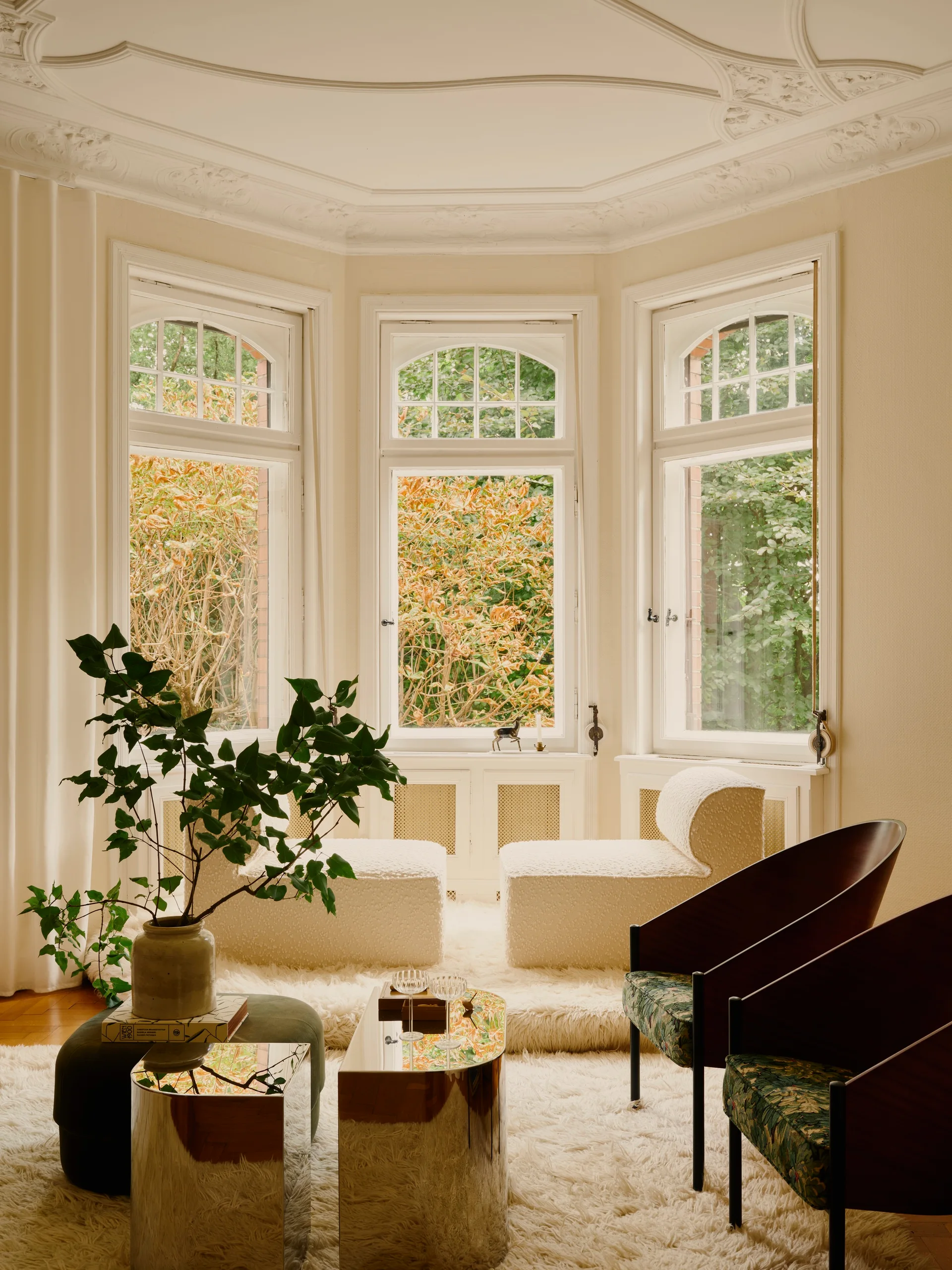 Cream lounge chairs and dark wood accent chairs around mirrored coffee tables on a shag rug in front of a classic bay window.