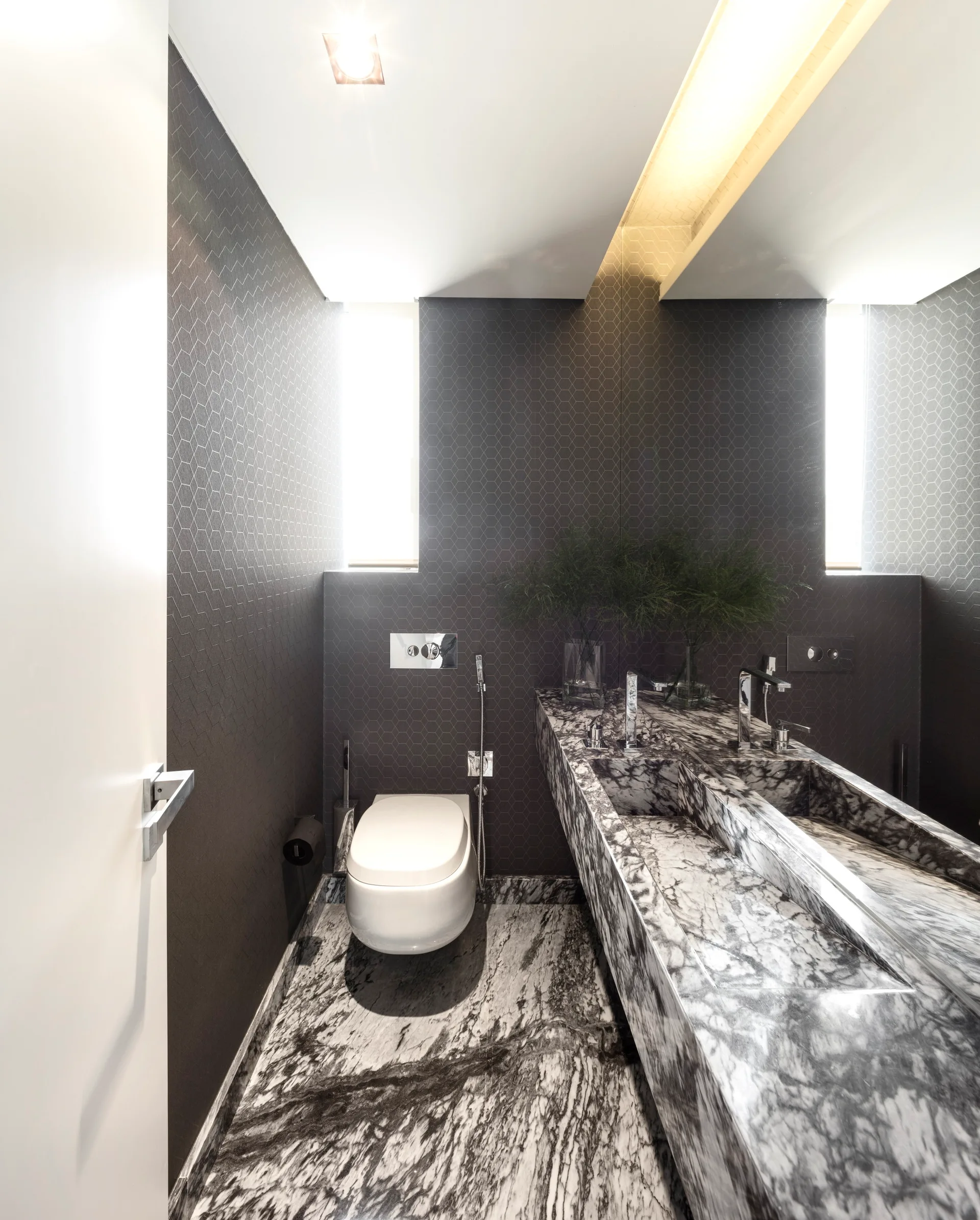 Modern powder room with dark hexagonal wall tiles, a wall-mounted toilet, and a matching black and white veined marble floor and vanity.