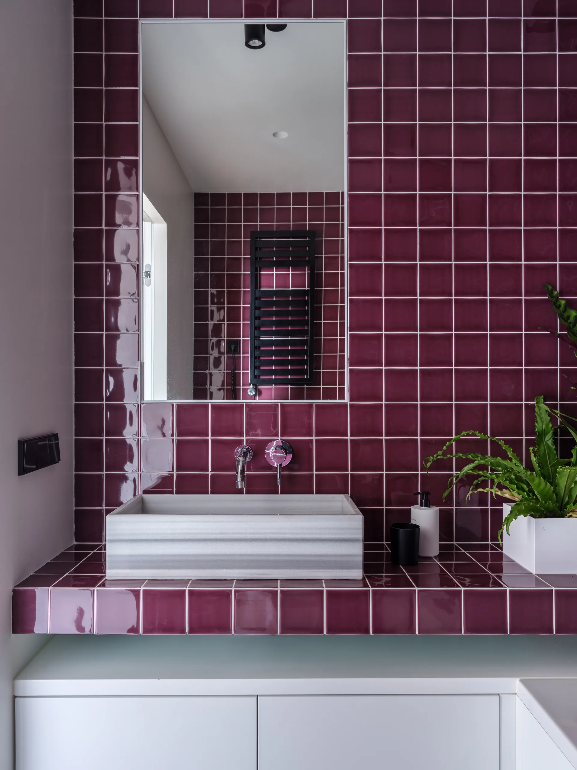 A rectangular striped stone vessel sink sits on a glossy burgundy tiled vanity beneath a rectangular wall mirror.