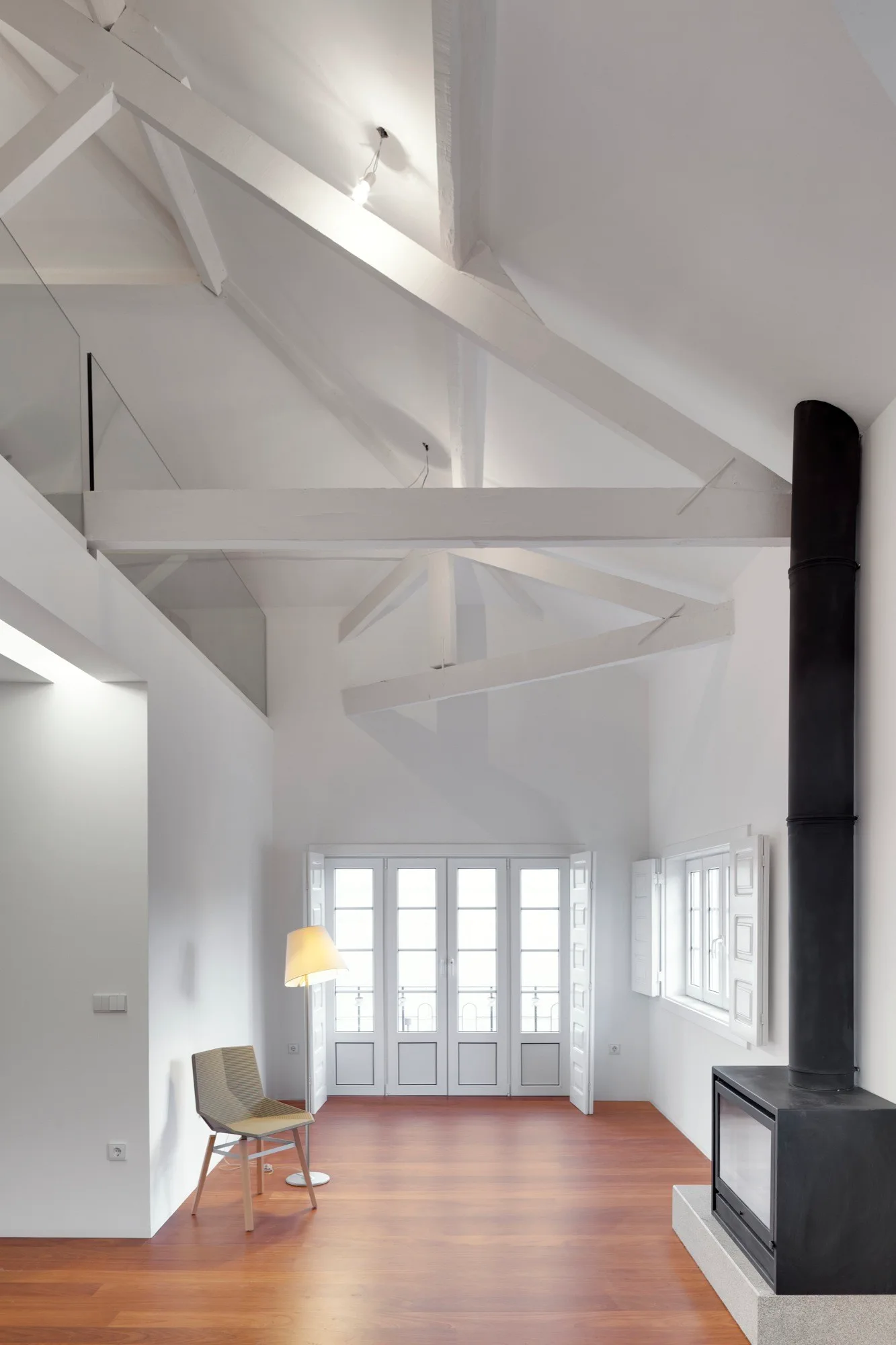 A minimalist living room with white vaulted ceilings, exposed beams, warm wood floors, a matte black fireplace, and white French doors.