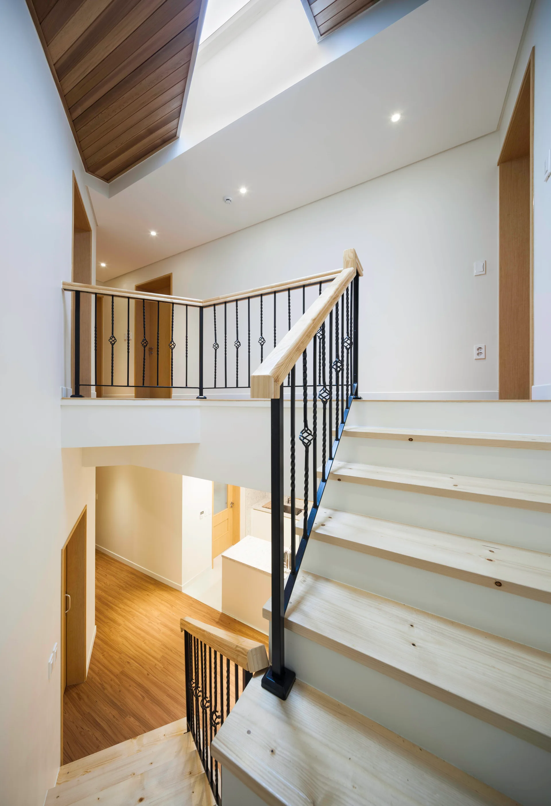 A modern multi-level staircase with light wood treads and black iron railings set against clean white walls.
