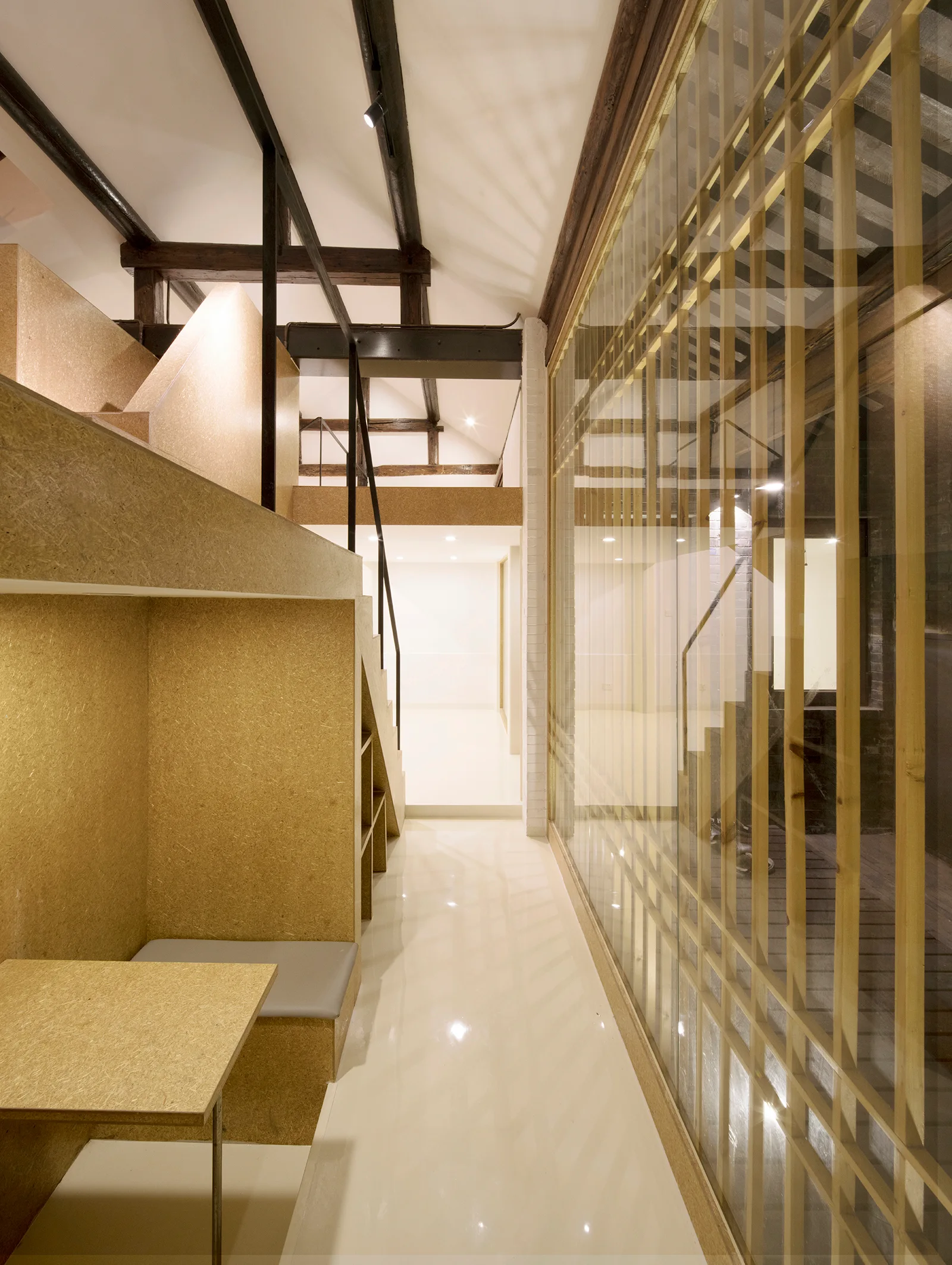 A modern interior corridor features a textured OSB wood loft structure with a desk, glossy white floors, and a floor-to-ceiling glass-slatted wall.