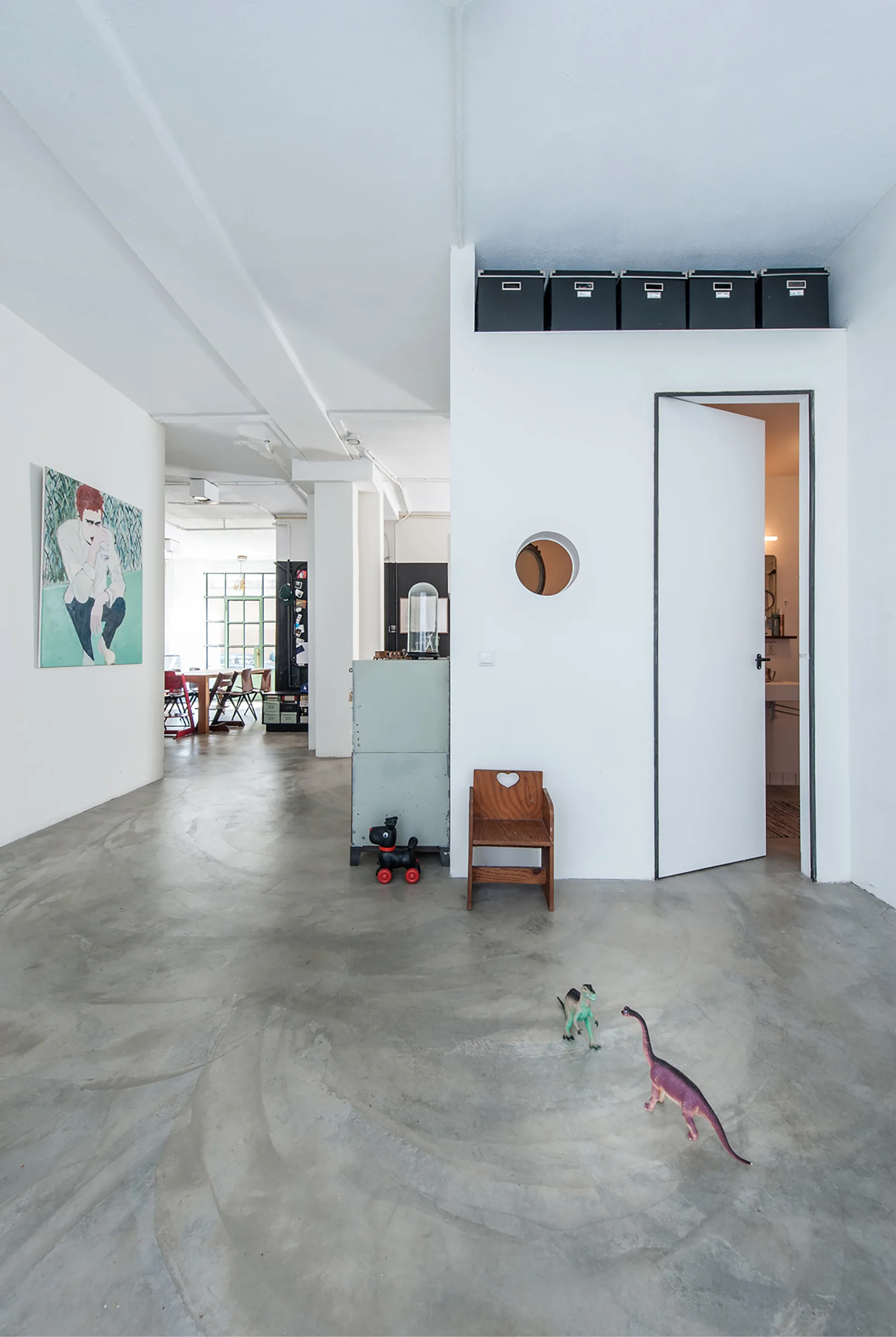An open loft space with swirled concrete flooring, a white partition wall featuring a circular cutout, and children's toys on the floor.